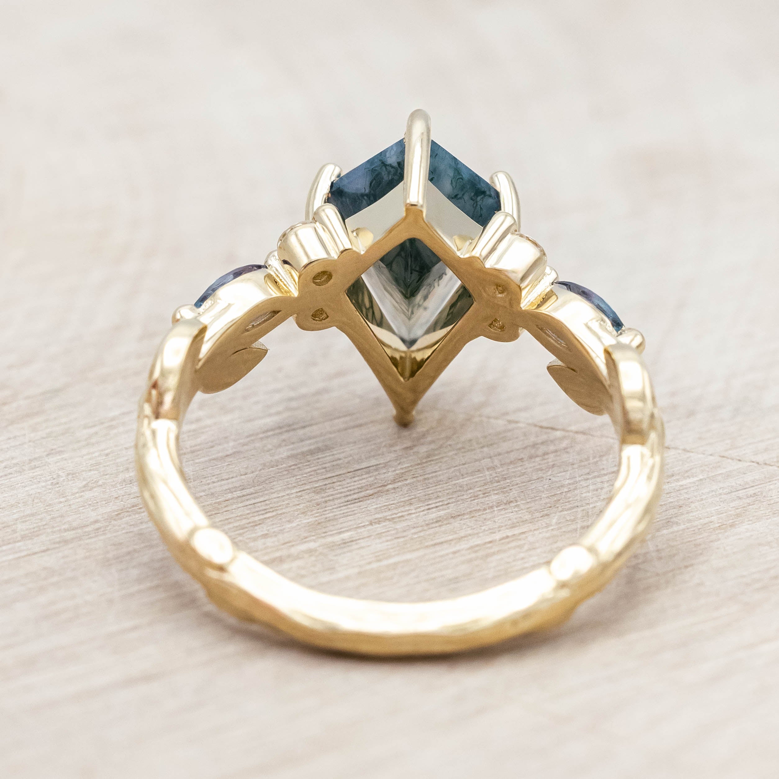 Gold ring with moss agate center stone with alexandrite & diamond accents on a light wooden surface