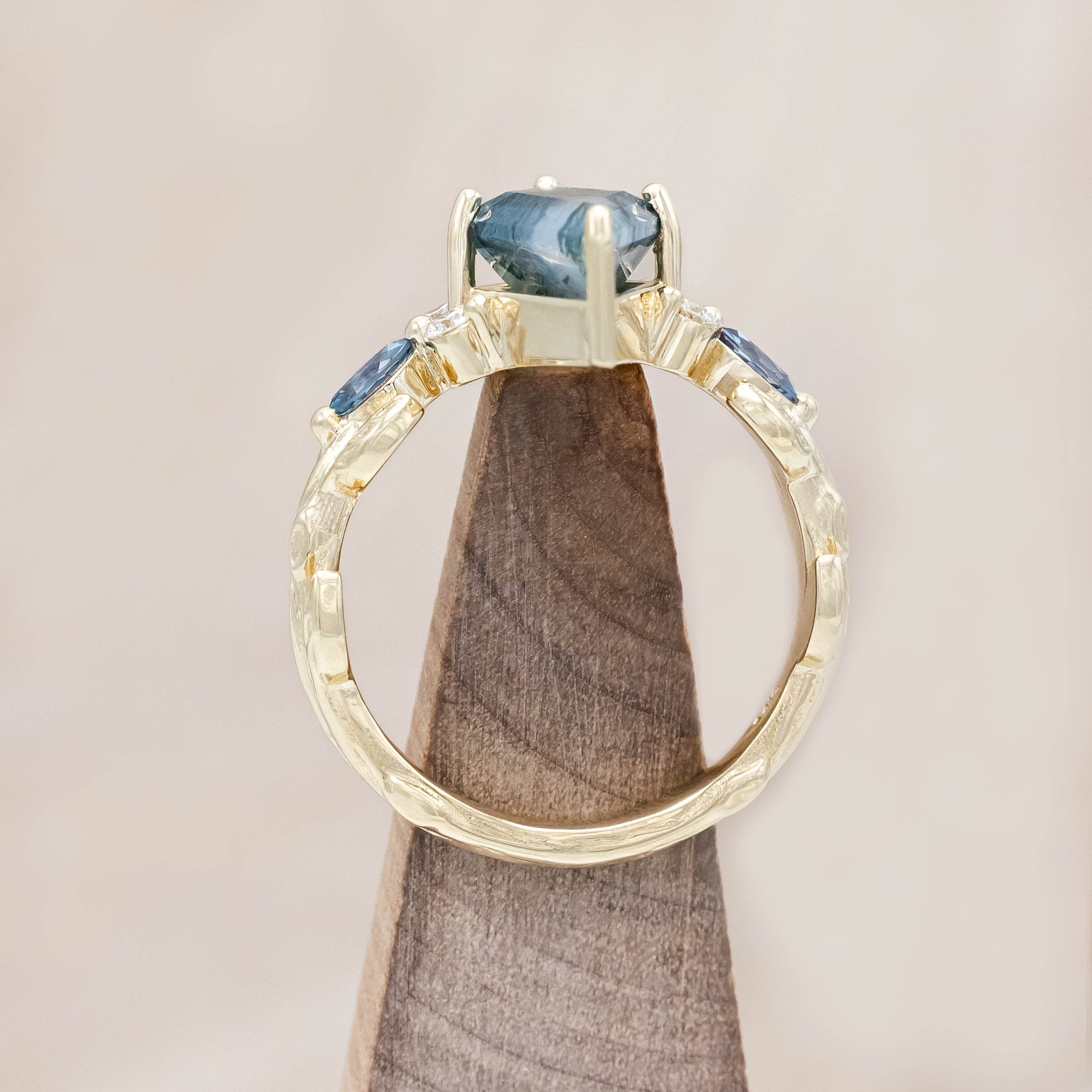 Gold ring with moss agate center stone with alexandrite & diamond accents on a light wooden surface