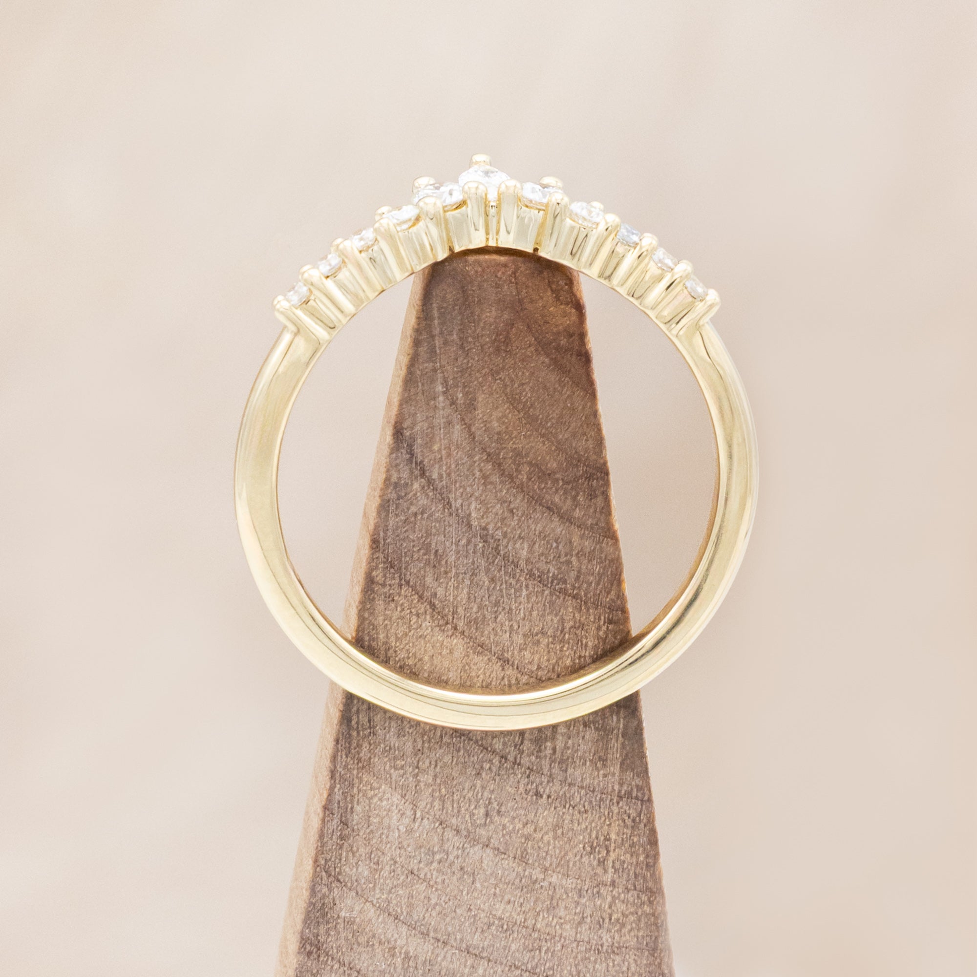 Gold ring with small diamonds on a wooden block against a beige background