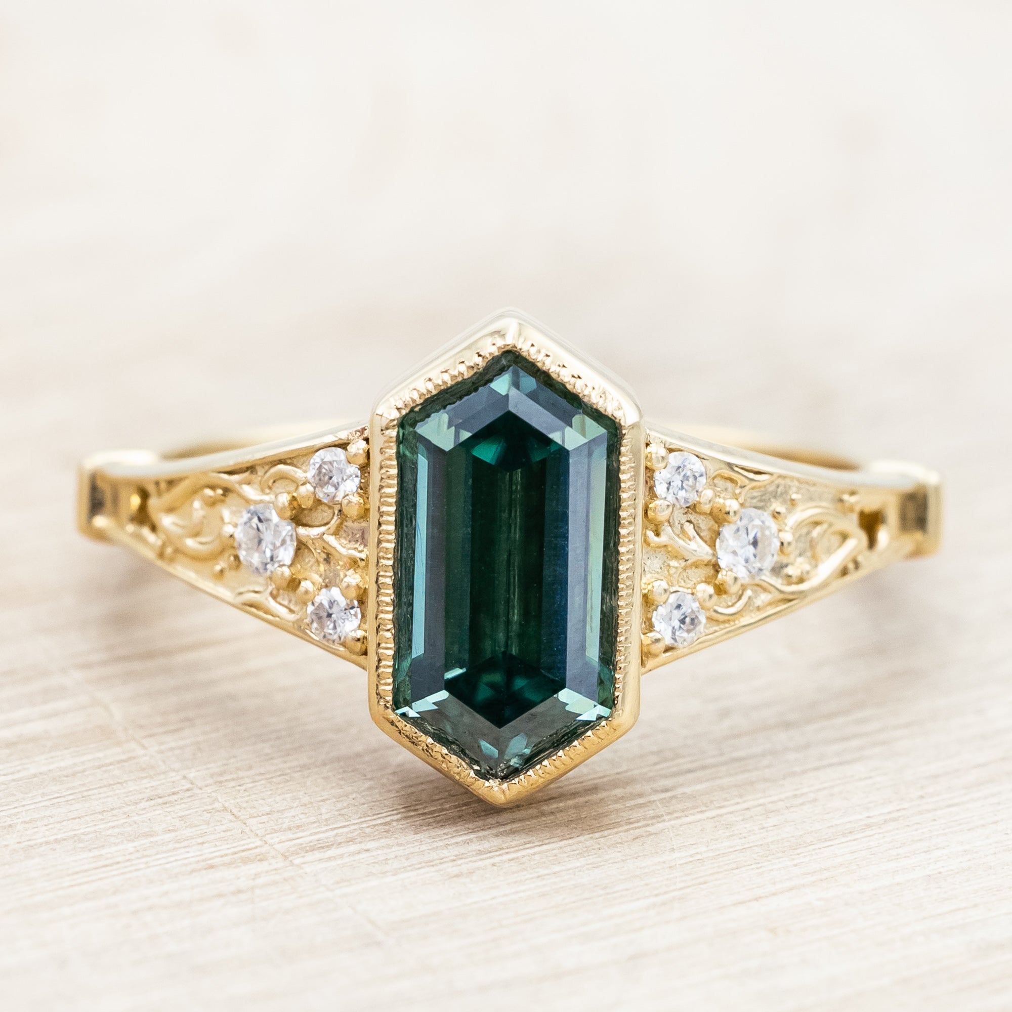 Gold ring with a green moissanite and diamond accents on a beige background