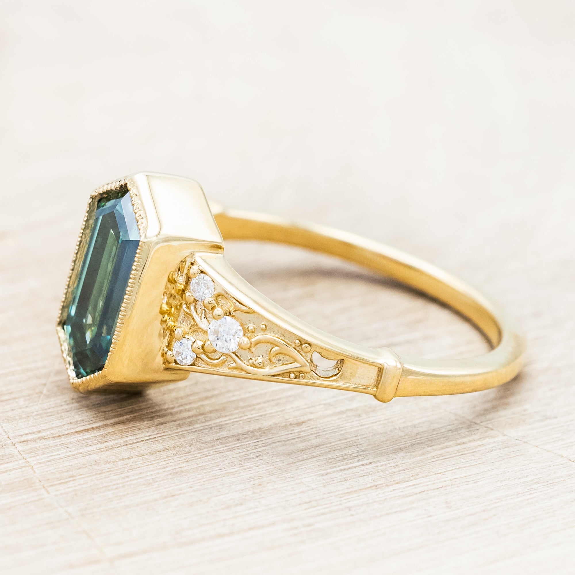 Gold ring with a green moissanite and diamond accents on a beige background