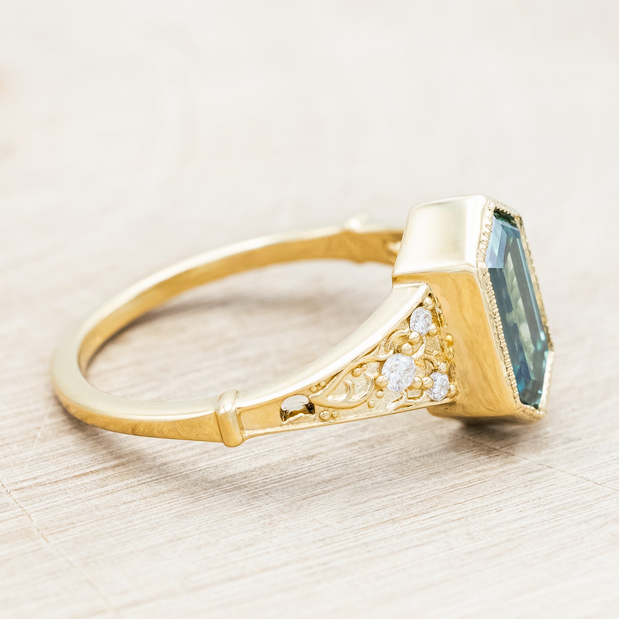 Gold ring with a green moissanite and diamond accents on a beige background