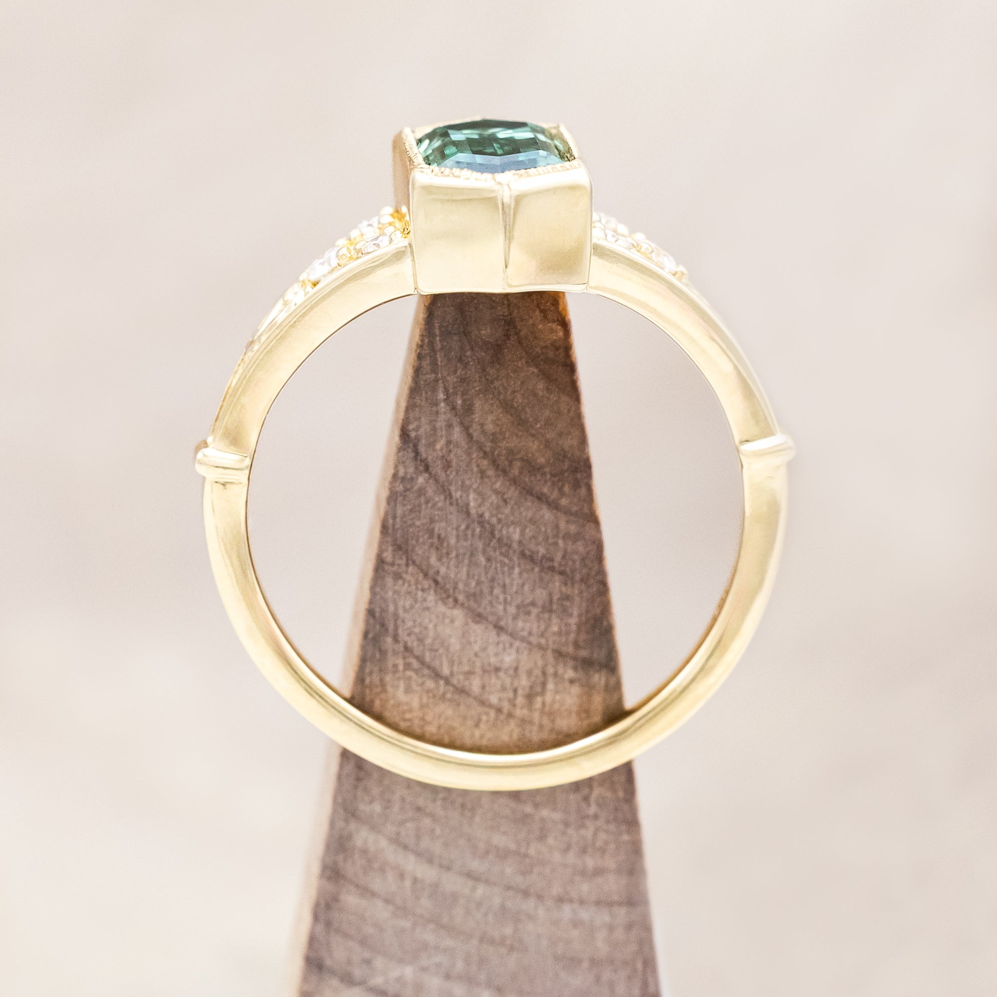 Gold ring with a green moissanite and diamond accents on a beige background