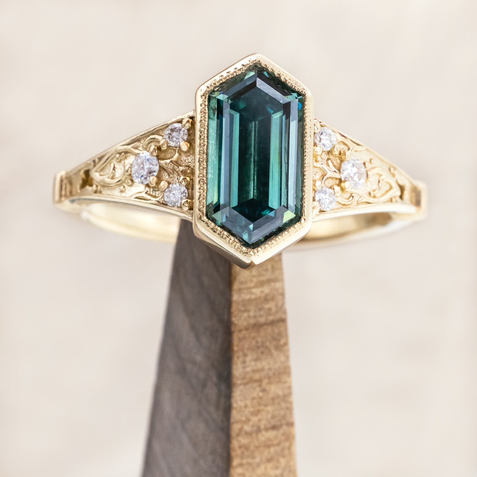 Gold ring with a green moissanite and diamond accents on a beige background
