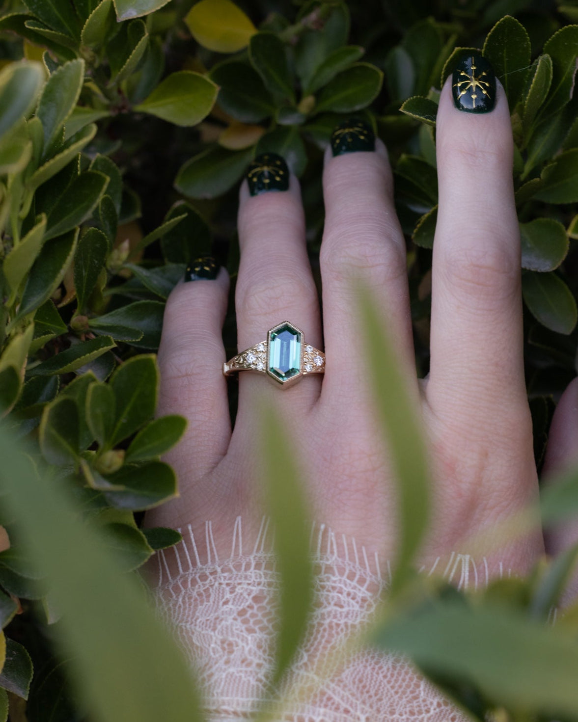 Hand with a green moissanite ring surrounded by green leaves
