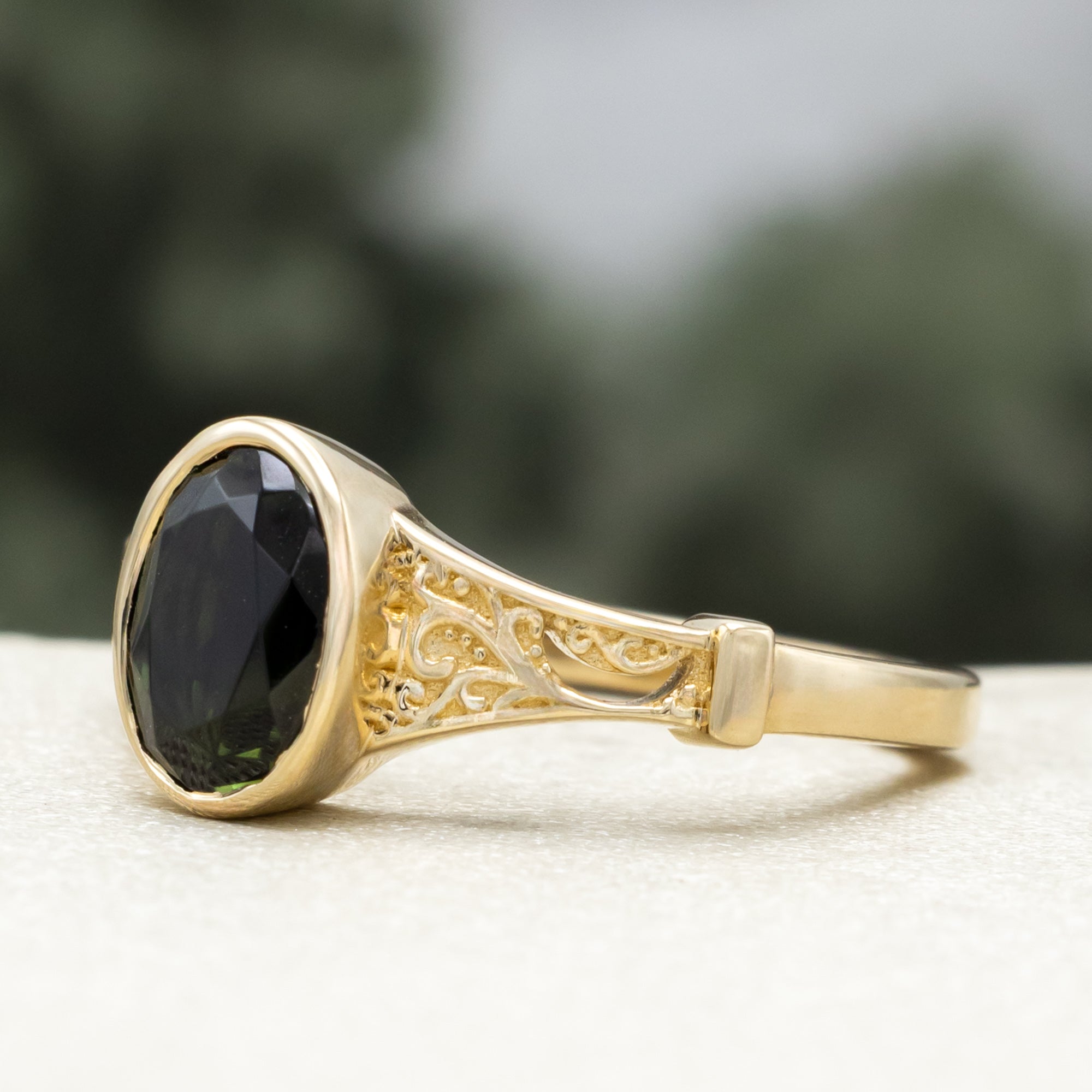 Gold ring with oval cut green tourmaline against a blurred green background