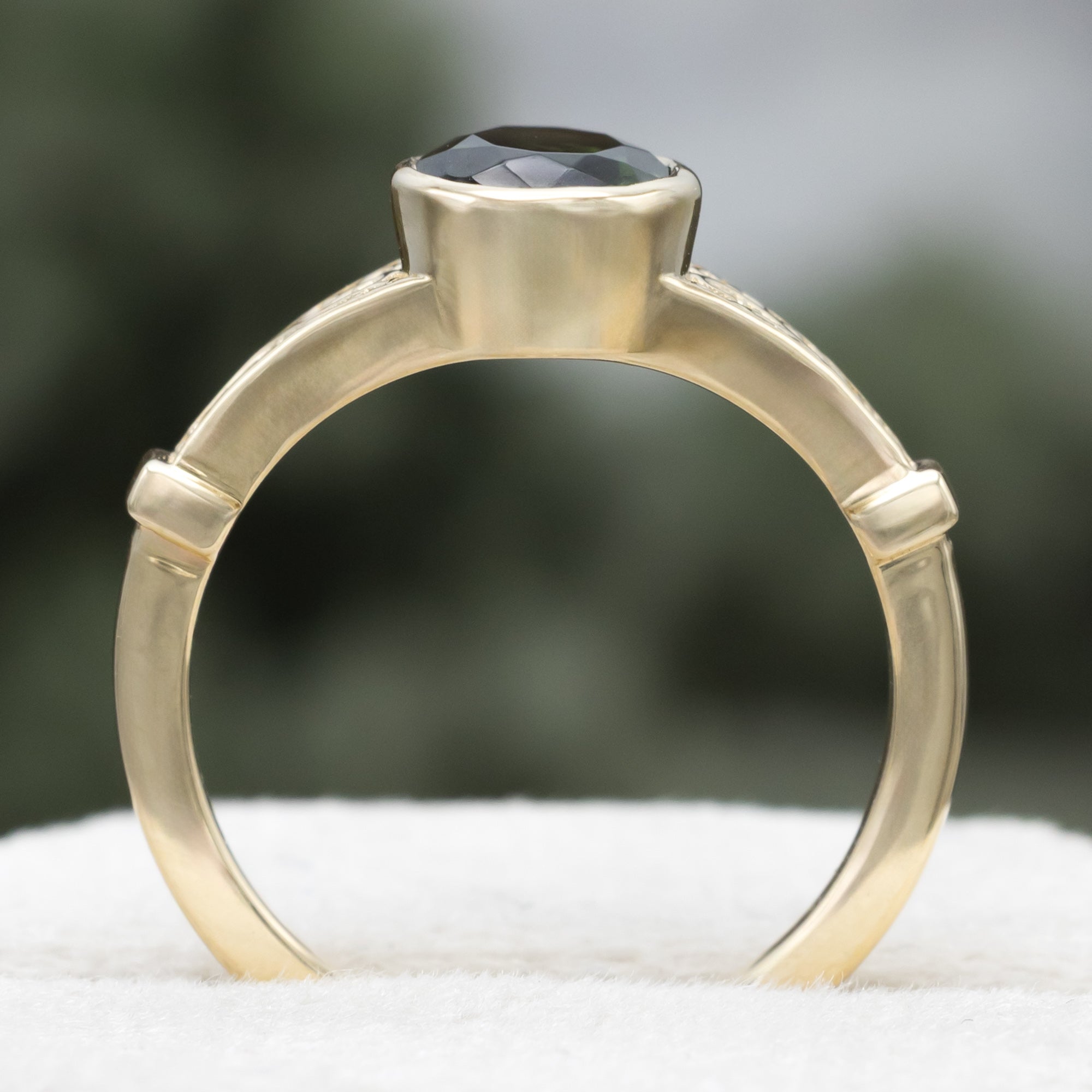 Gold ring with oval cut green tourmaline against a blurred green background