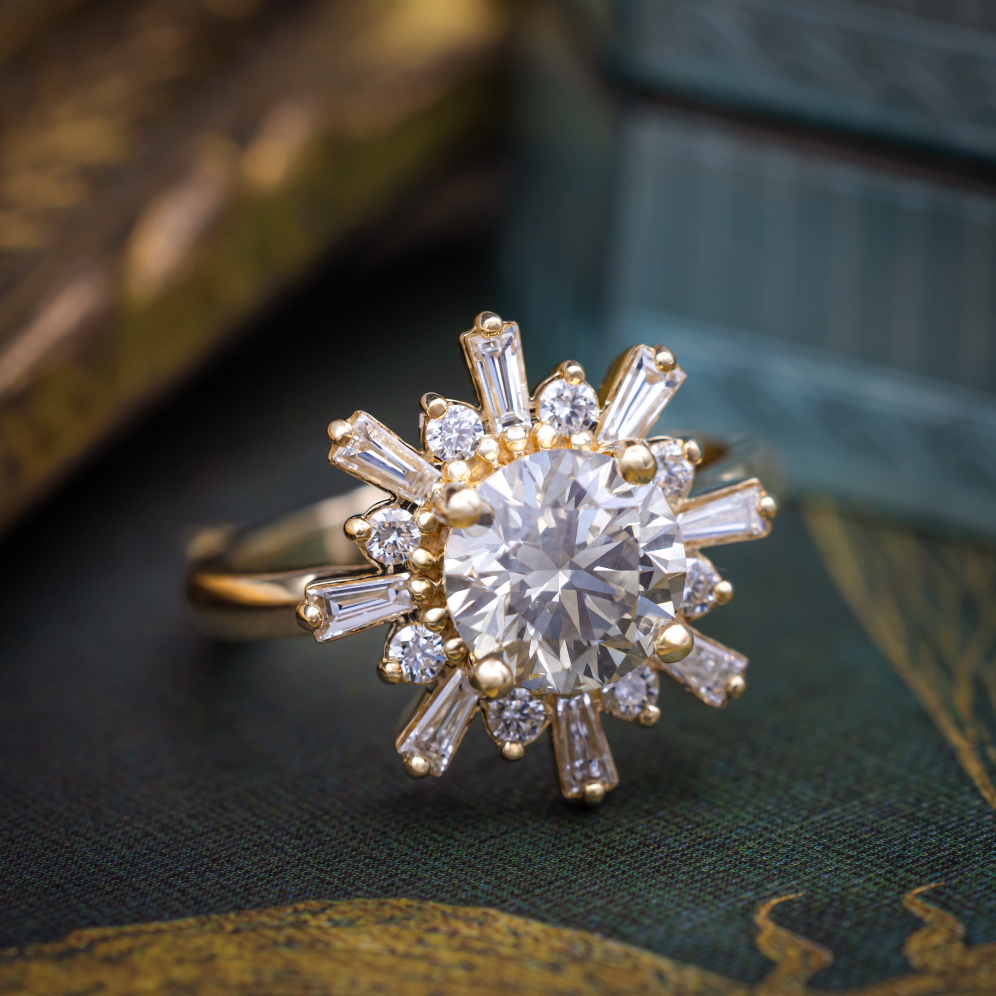 A yellow gold ring with salt & pepper diamond center stone and diamond accents on a dark blurred decorative surface