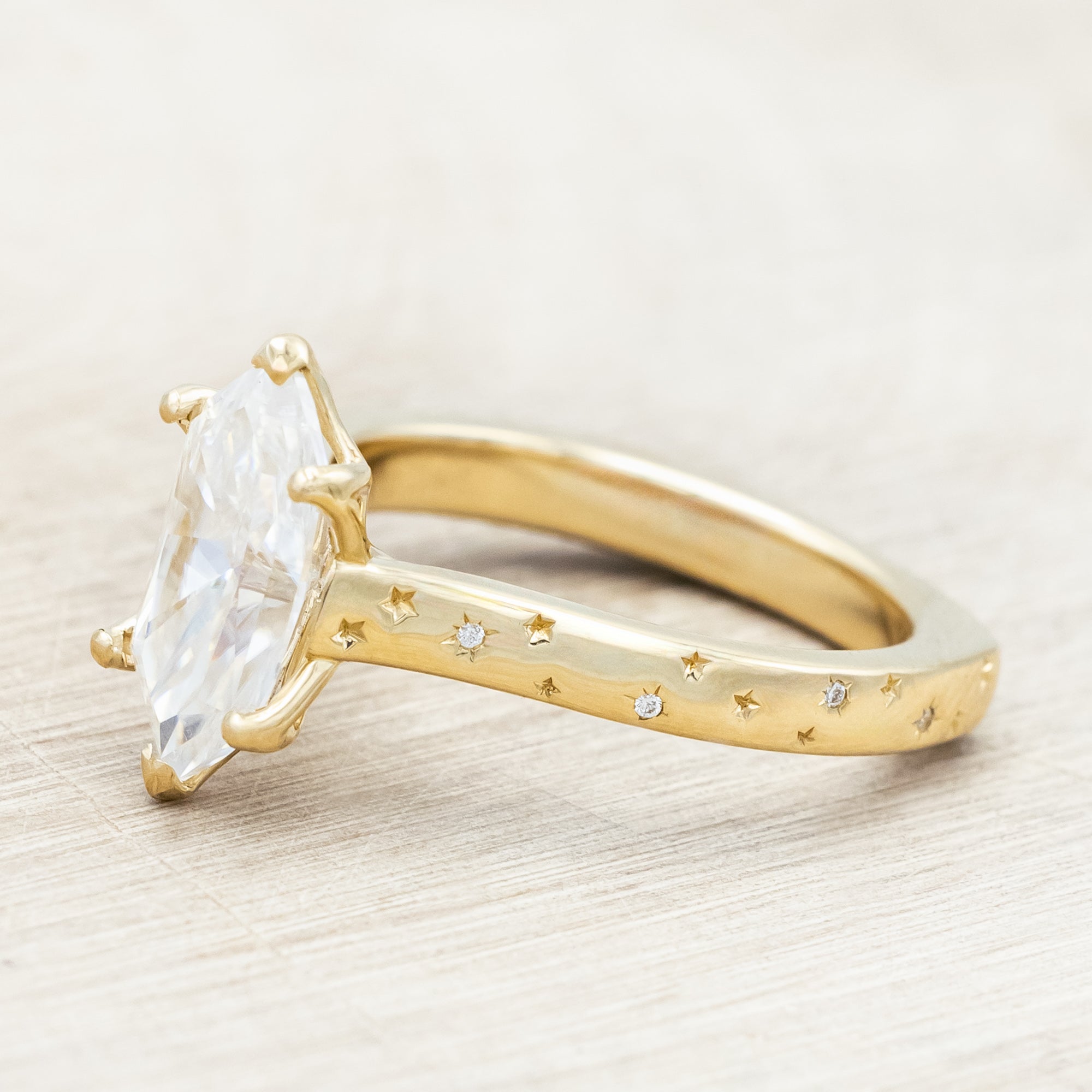 Gold ring with a moissanite center stone on a wooden stand against a neutral background