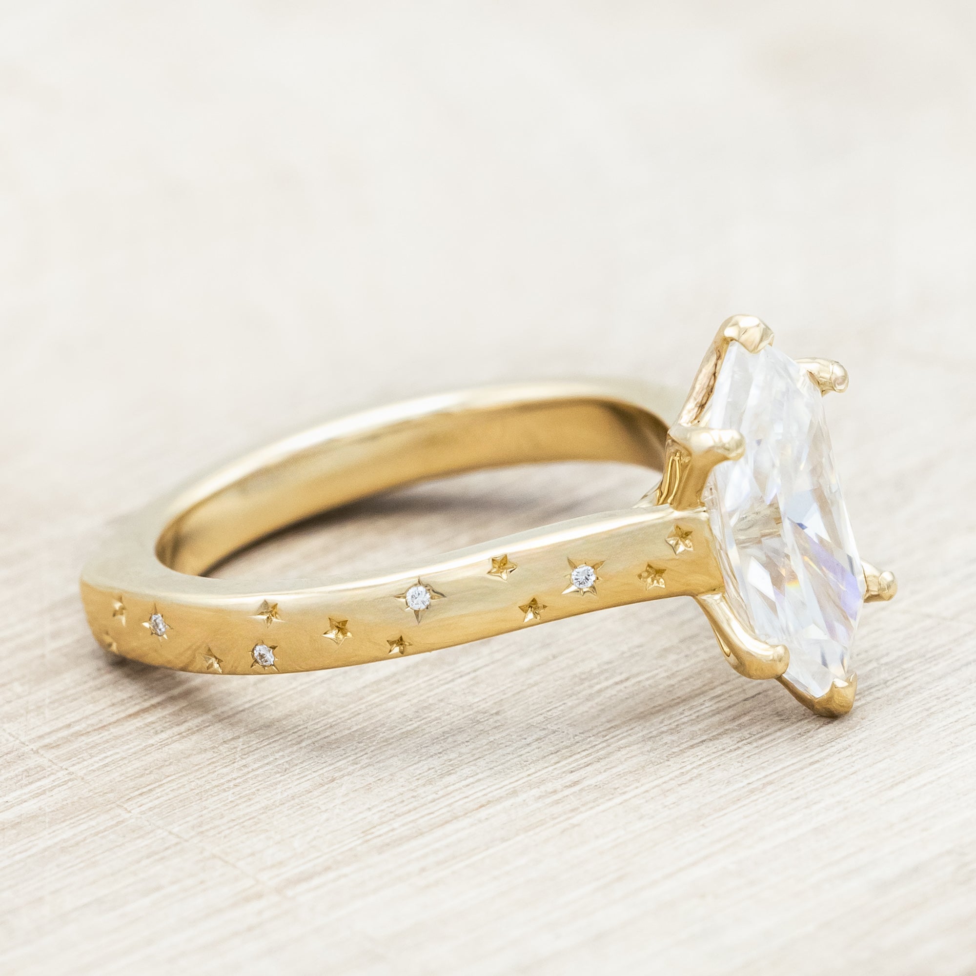 Gold ring with a moissanite center stone on a wooden stand against a neutral background