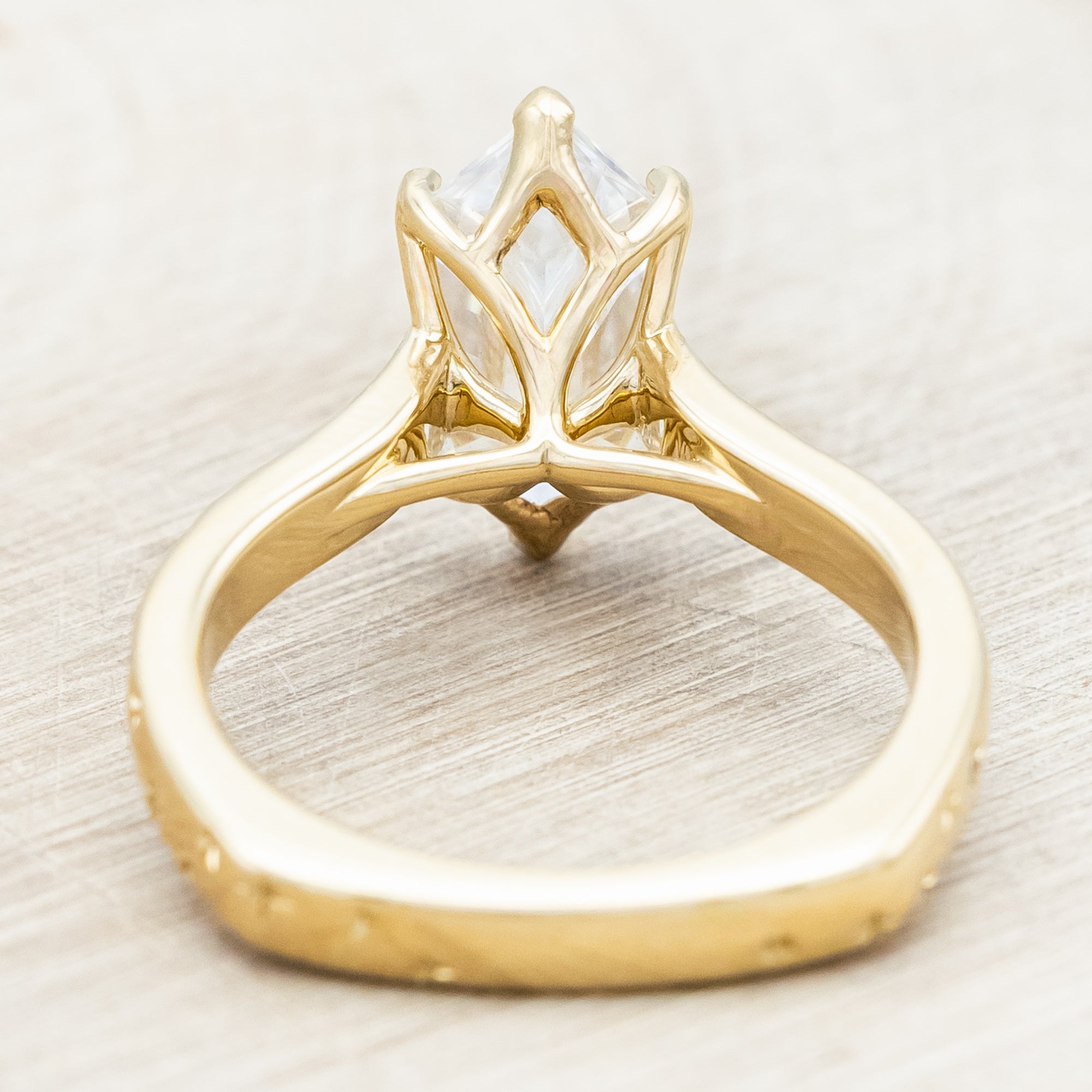 Gold ring with a moissanite center stone on a wooden stand against a neutral background