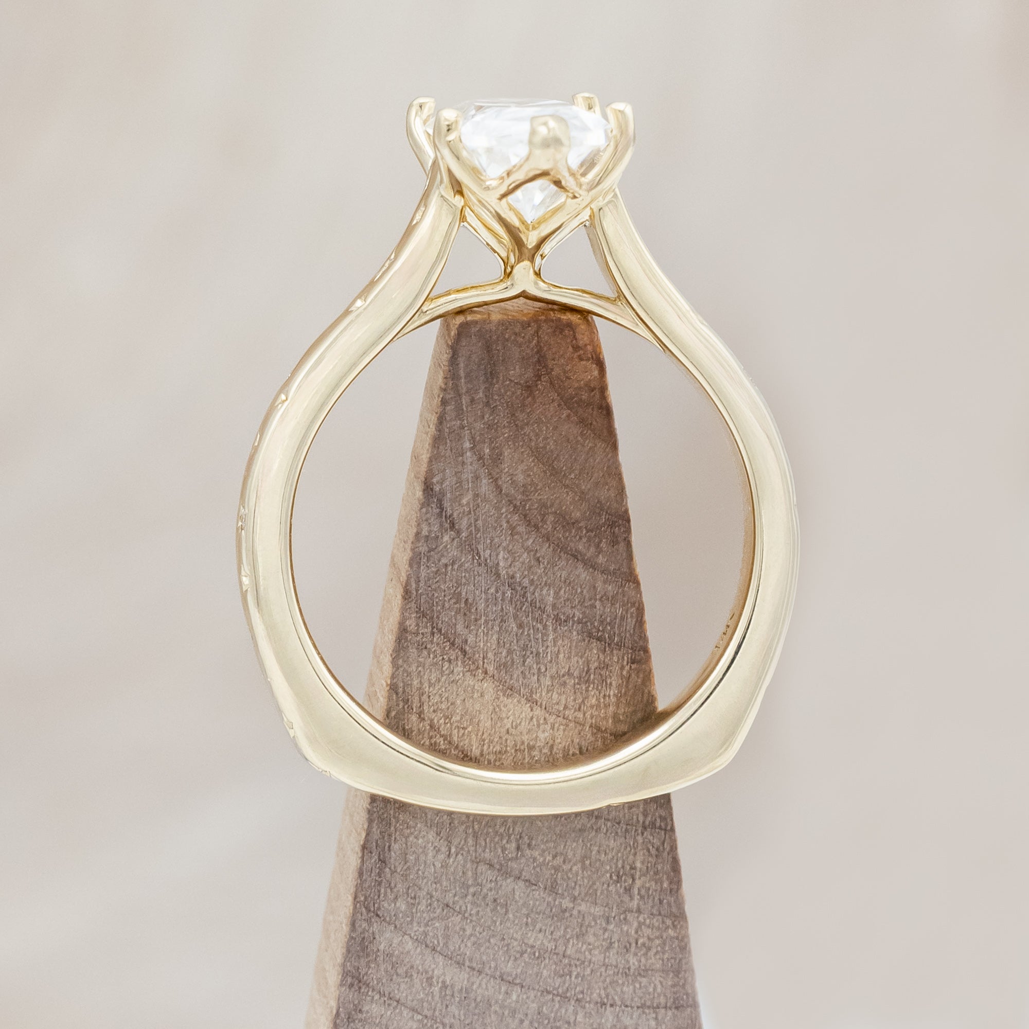 Gold ring with a moissanite center stone on a wooden stand against a neutral background