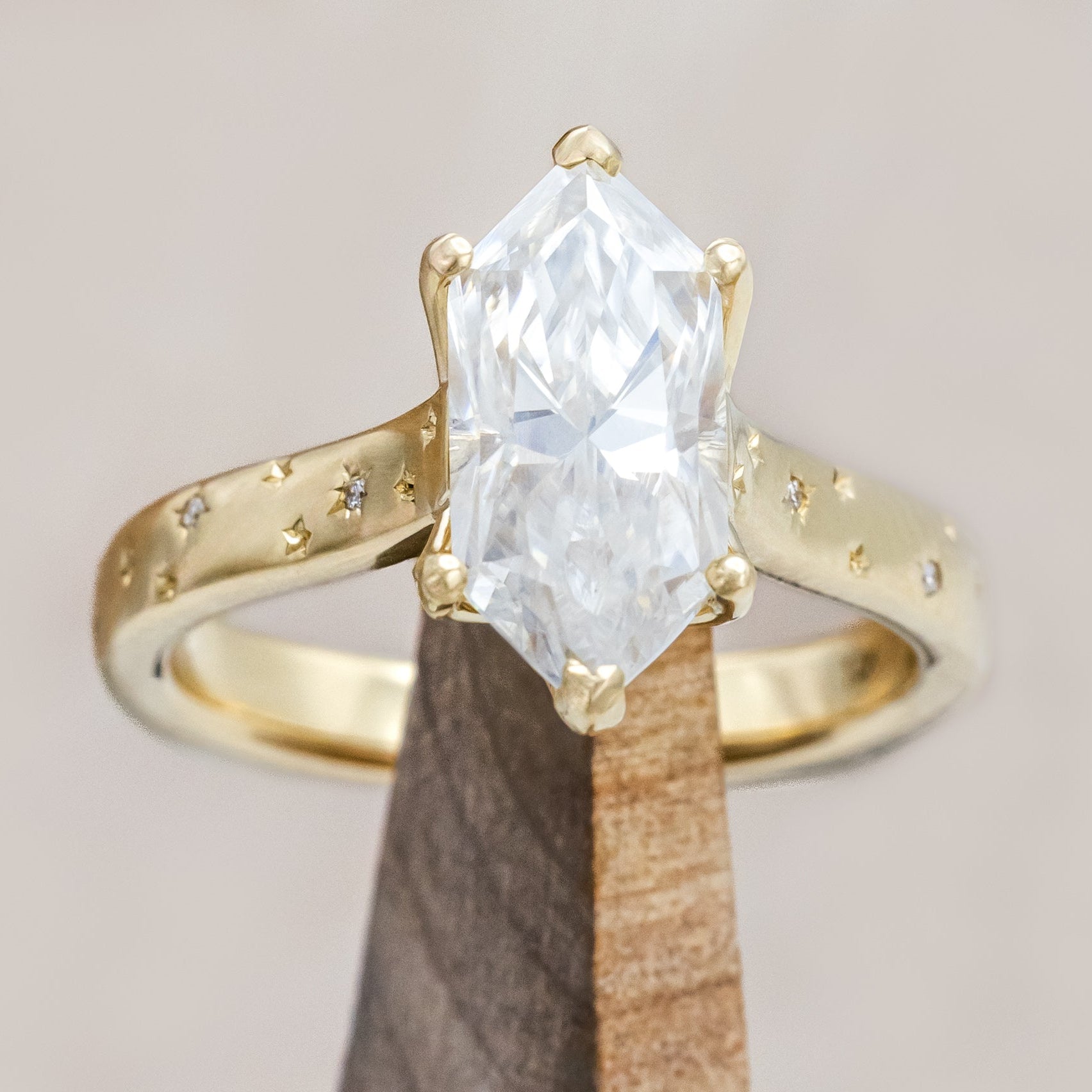 Gold ring with a moissanite center stone on a wooden stand against a neutral background