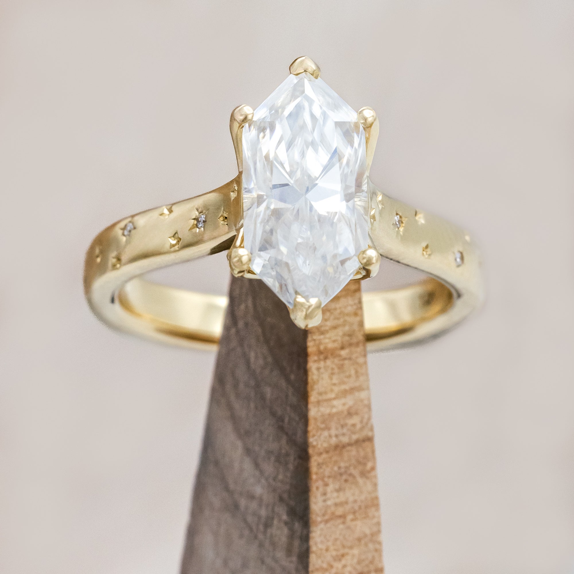 Gold ring with a moissanite center stone on a wooden stand against a neutral background