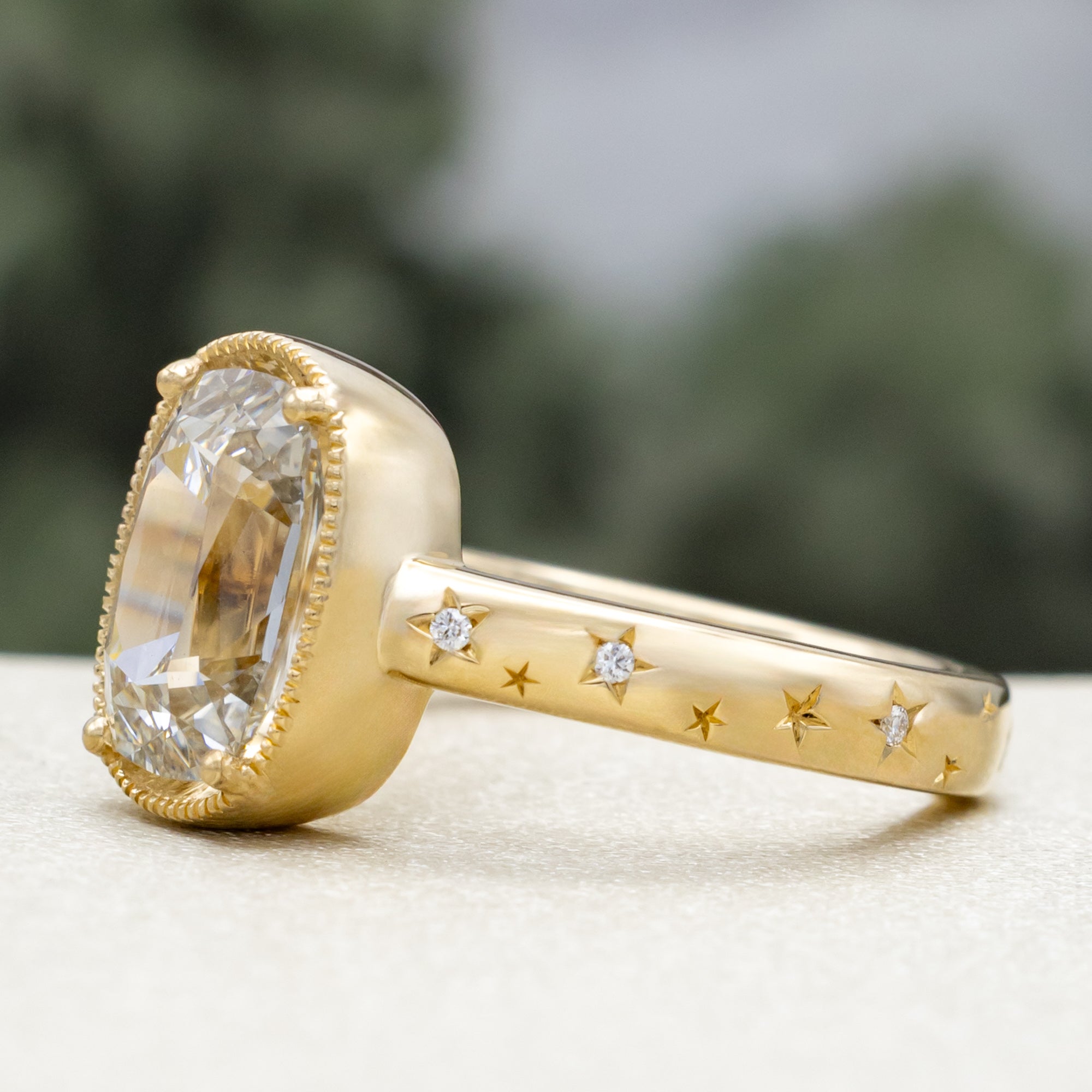 Gold ring with a lab diamond center stone and diamond accents on the band against a blurred green background