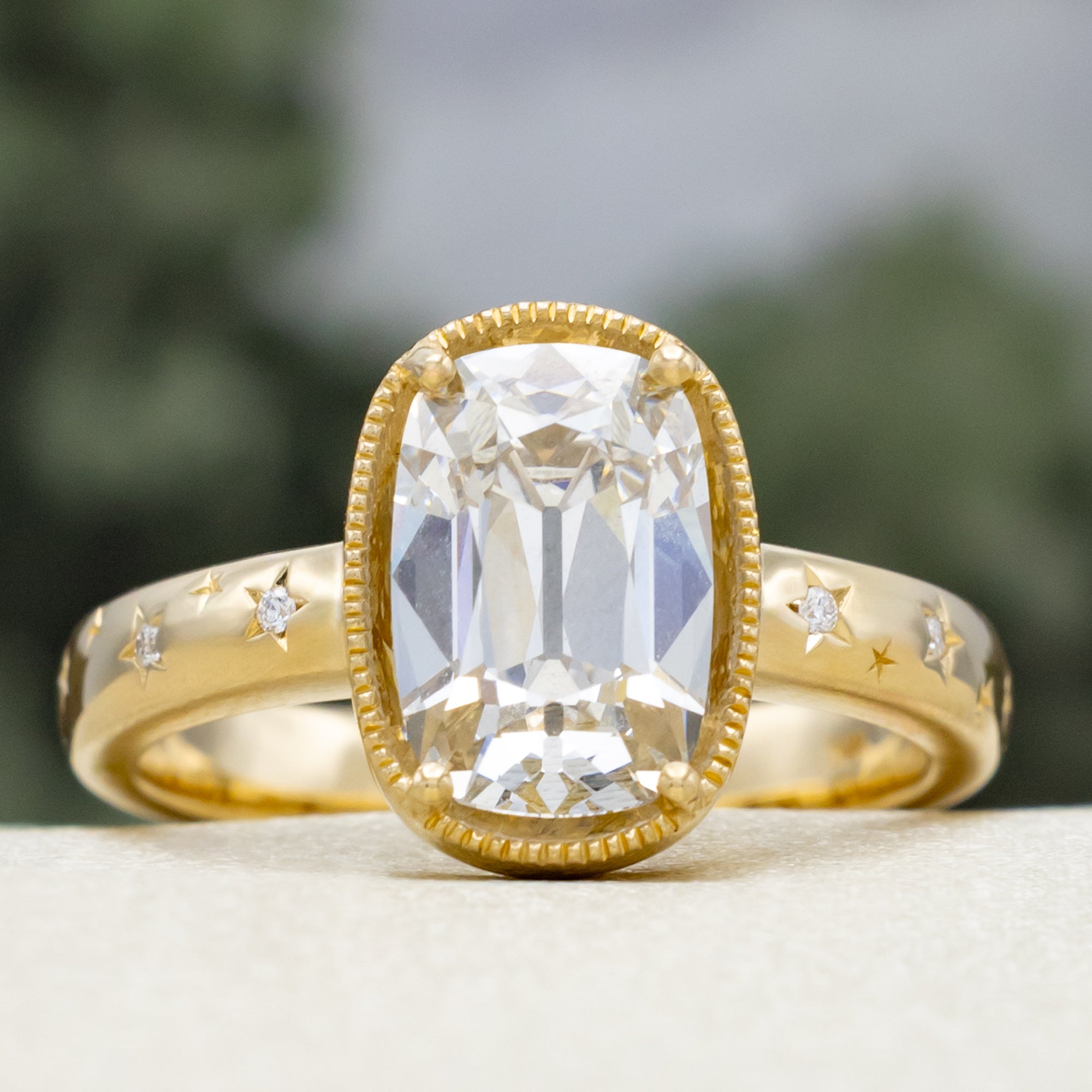 Gold ring with a lab diamond center stone and diamond accents on the band against a blurred green background
