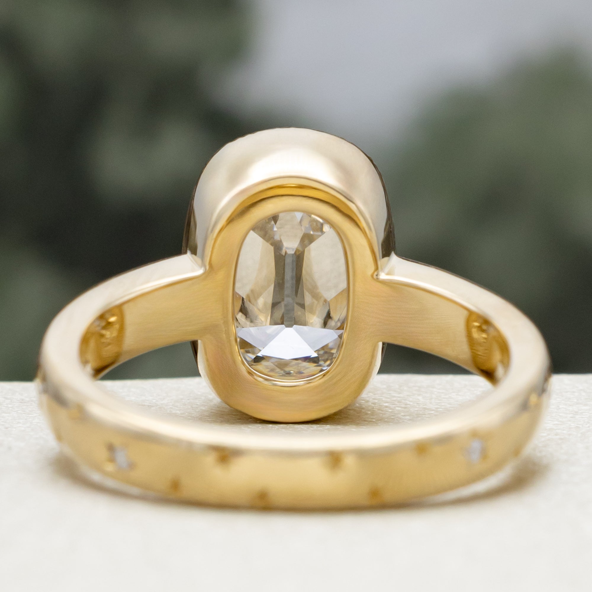 Gold ring with a lab diamond center stone and diamond accents on the band against a blurred green background