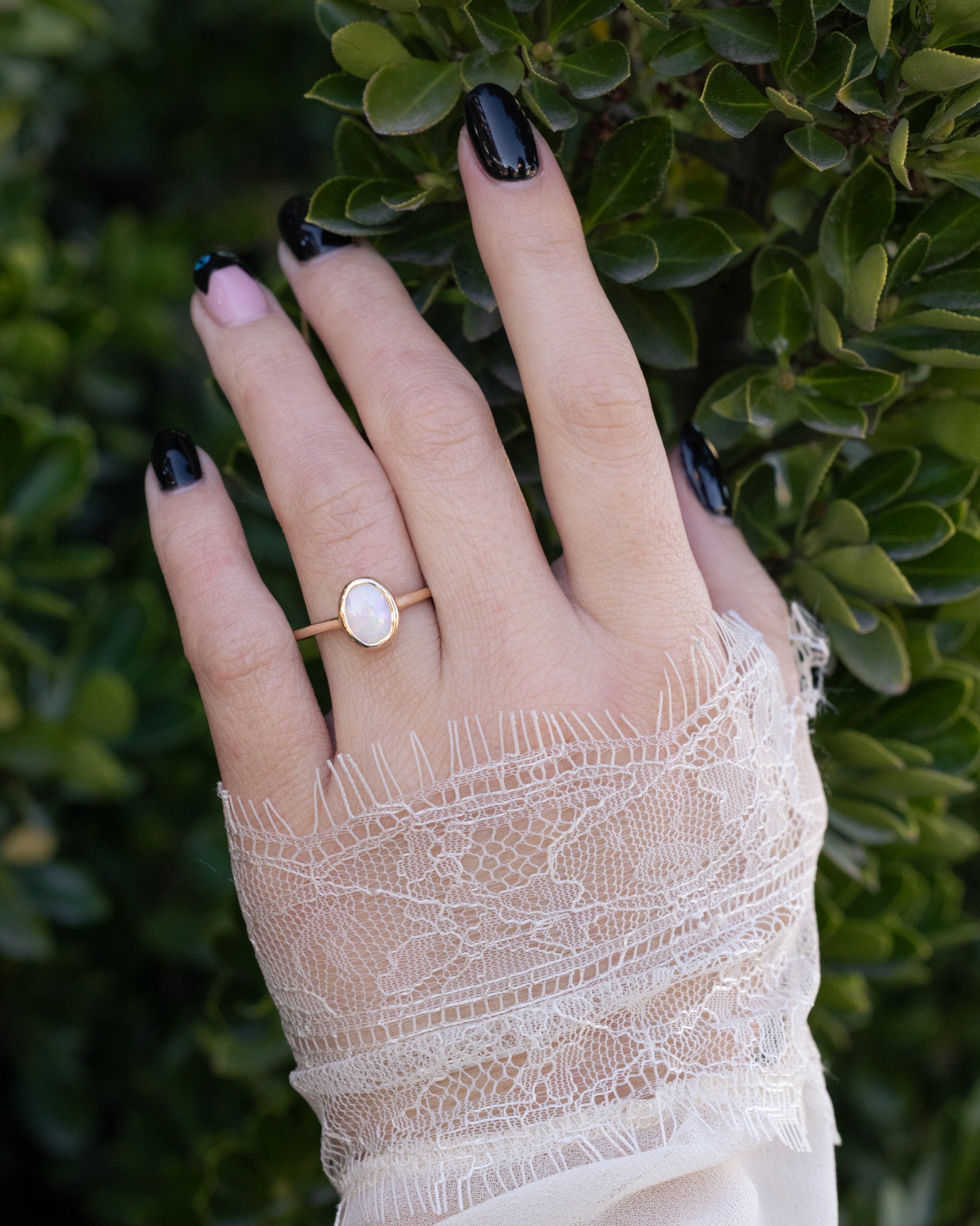 Hand wearing a gold ring with a white opal against a green leafy background