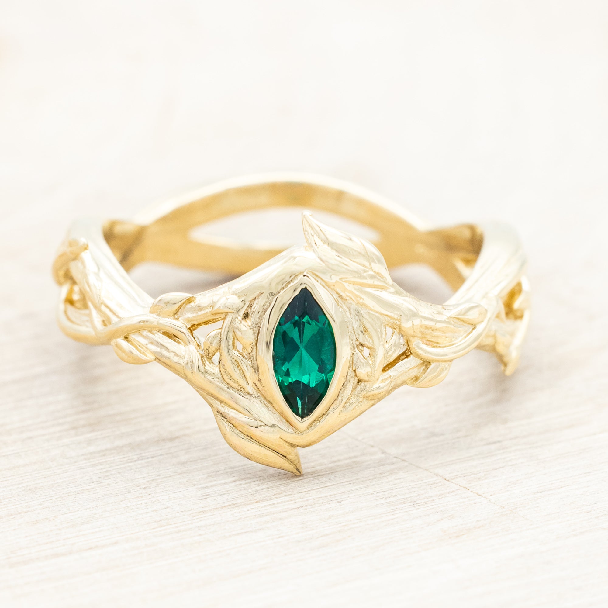 Gold ring with a green lab emerald against a light wooden background