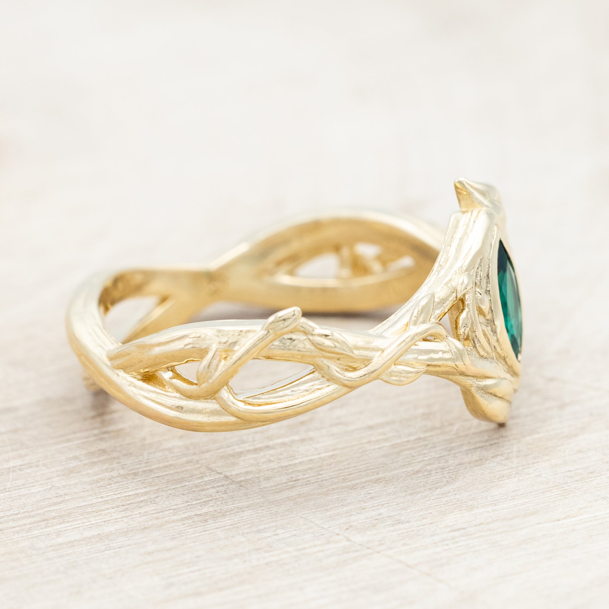 Gold ring with a green lab emerald against a light wooden background