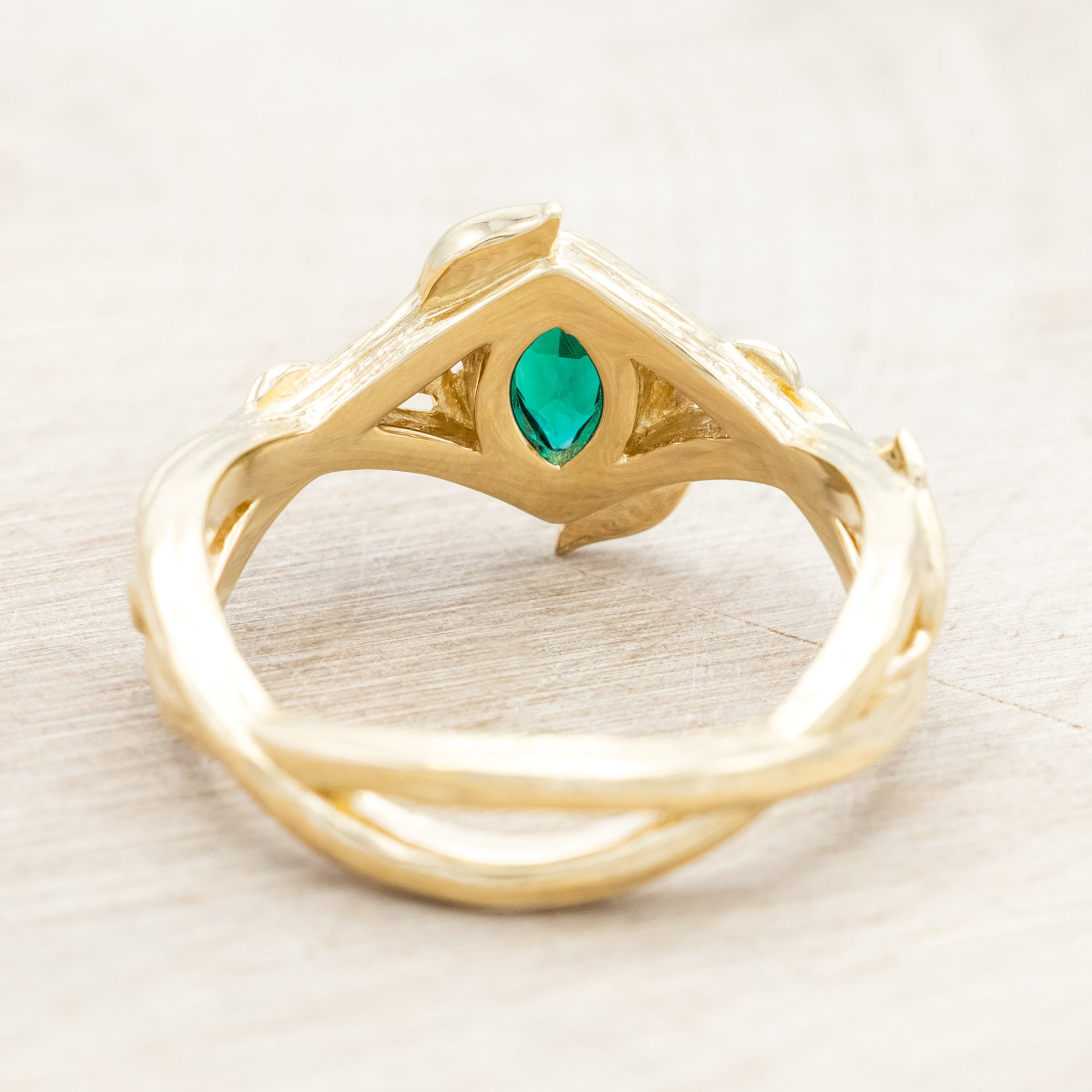 Gold ring with a green lab emerald against a light wooden background