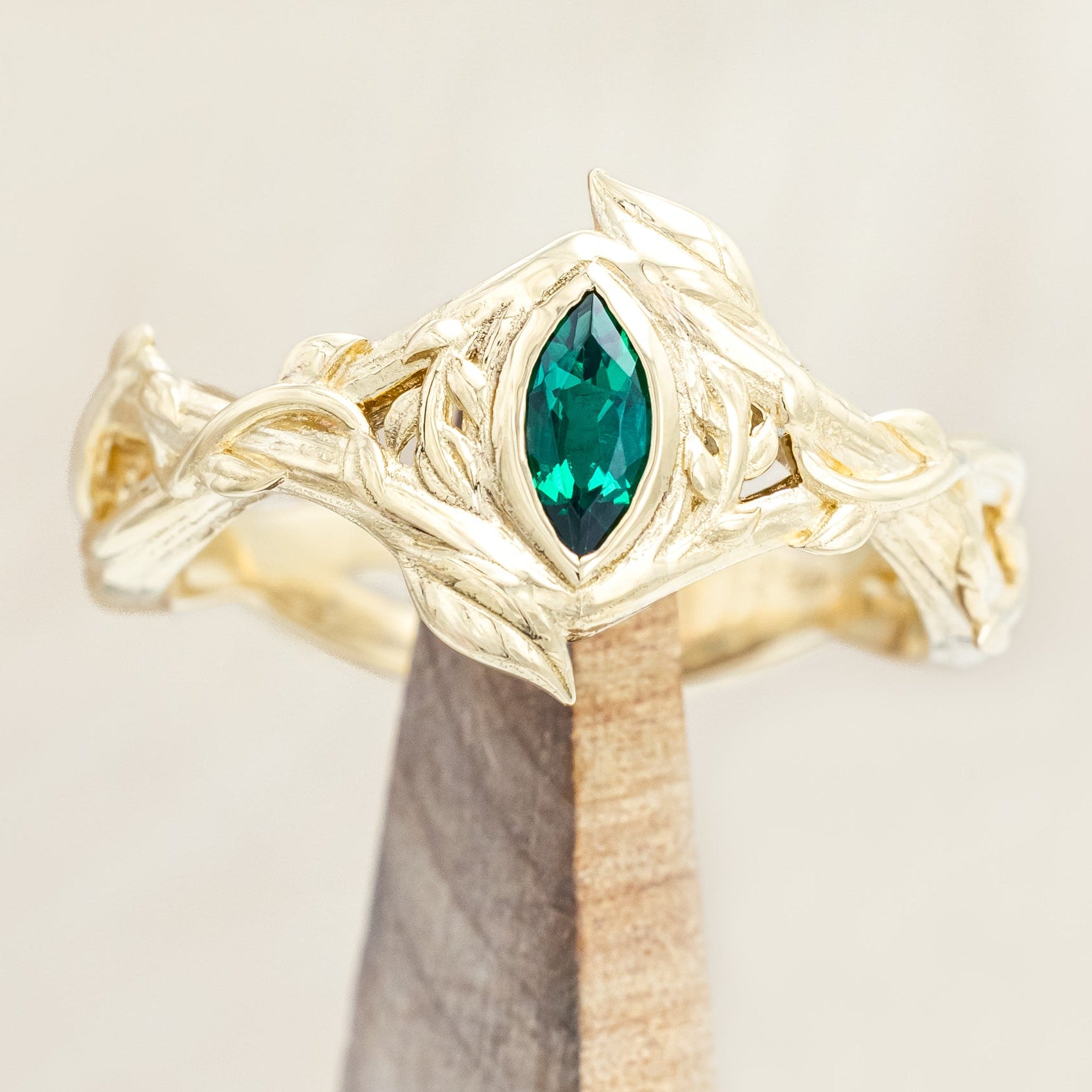 Gold ring with a green lab emerald on a wooden stand against a beige background