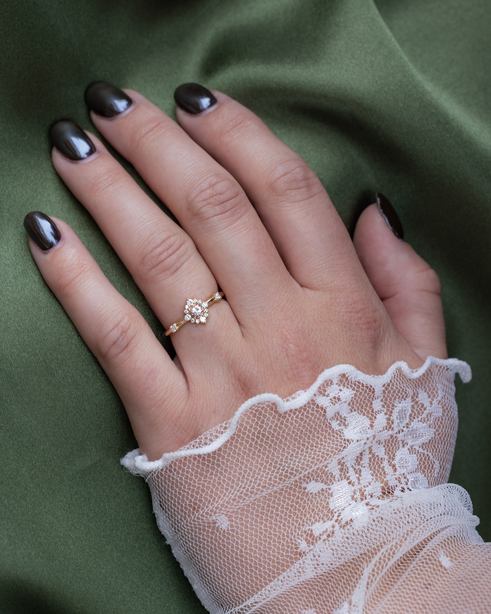 Hand wearing a delicate ring with lace sleeve on a green fabric background