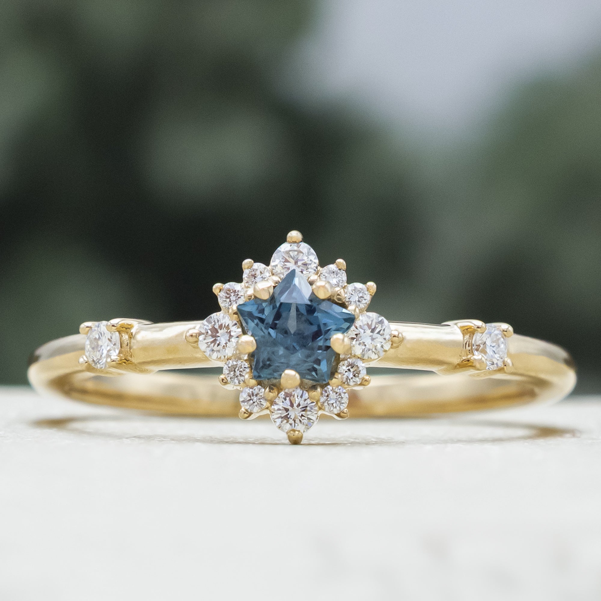 Gold ring with a blue star-shaped sapphire and diamond accents on a blurred green background