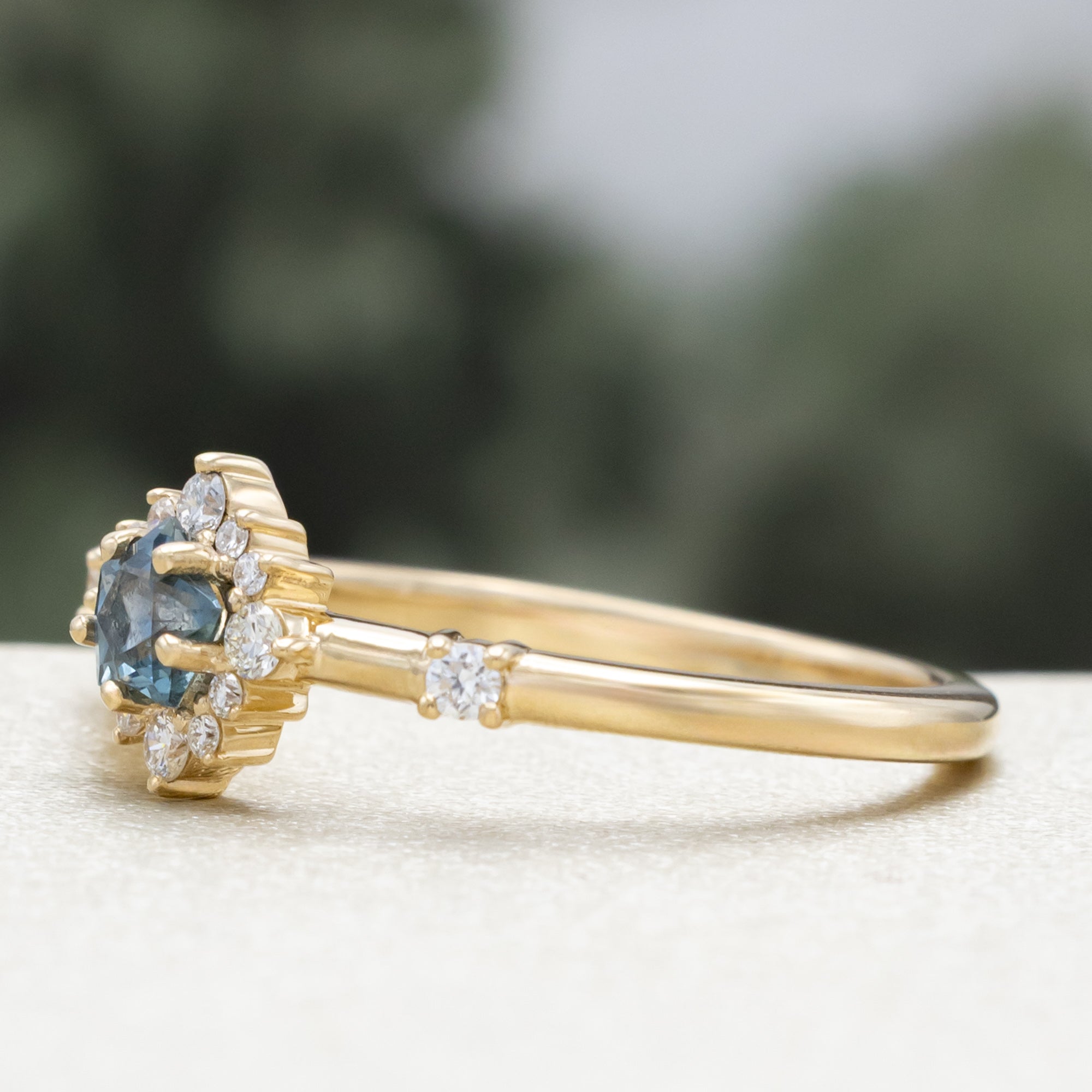 Gold ring with a blue star-shaped sapphire and diamond accents on a blurred green background