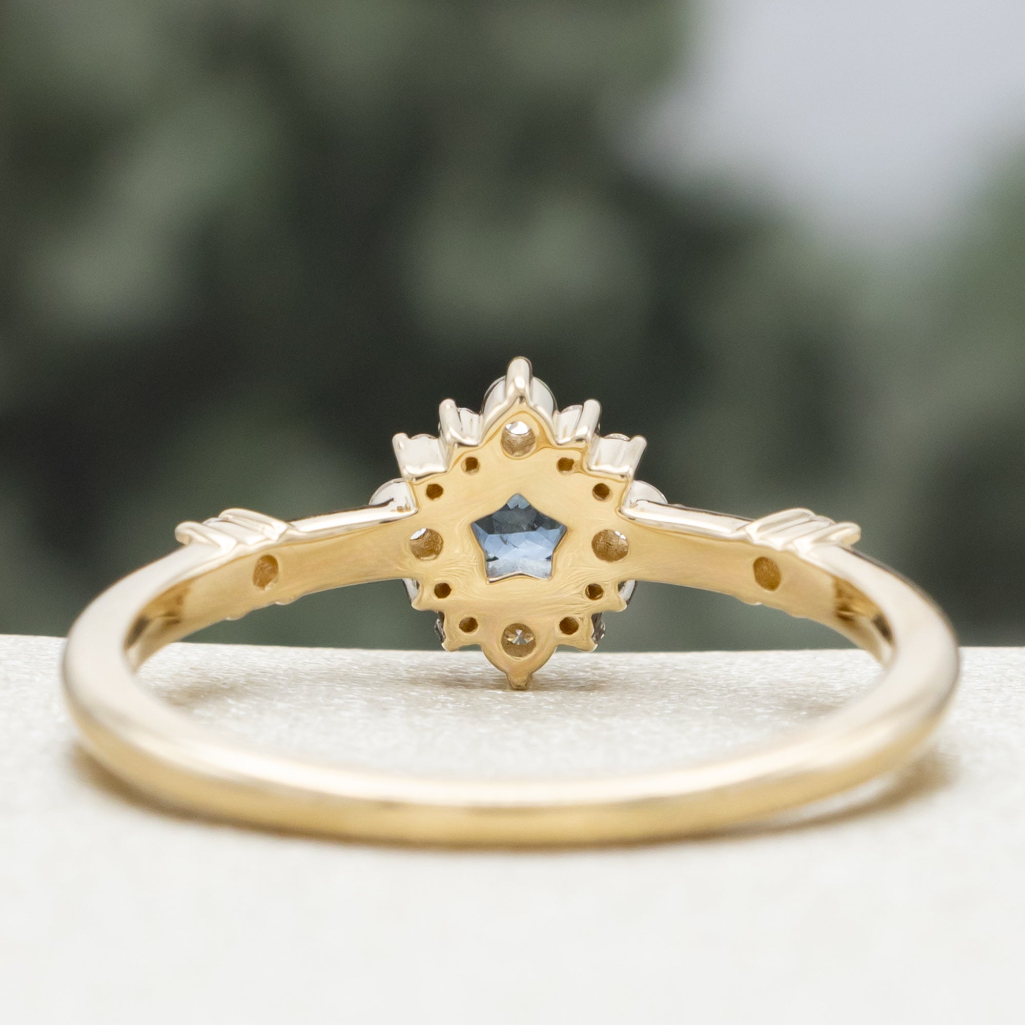 Gold ring with a blue star-shaped sapphire and diamond accents on a blurred green background