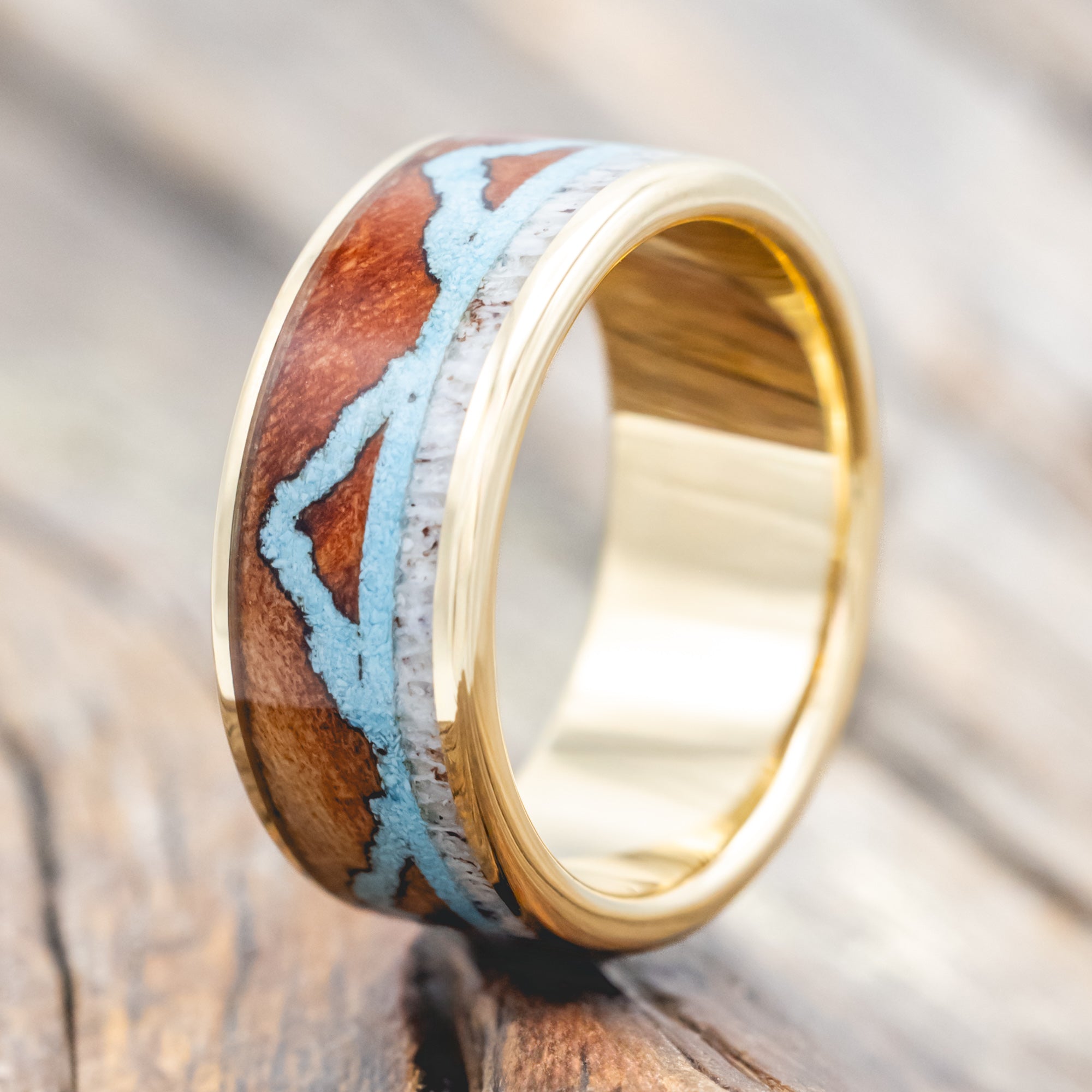 Yellow gold ring with whiskey barrel, antler, and turquoise mountains on a wooden surface