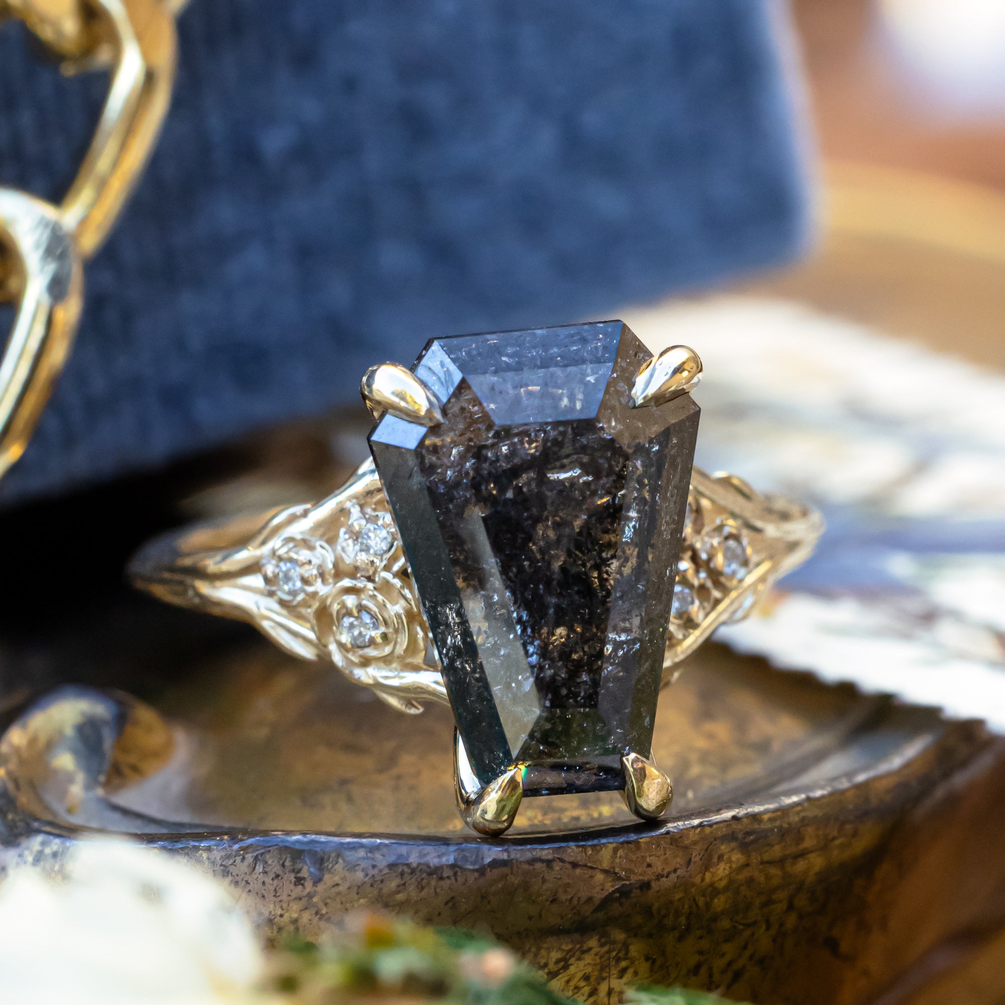 Gold ring with a large black salt & pepper diamond on a decorative stand.