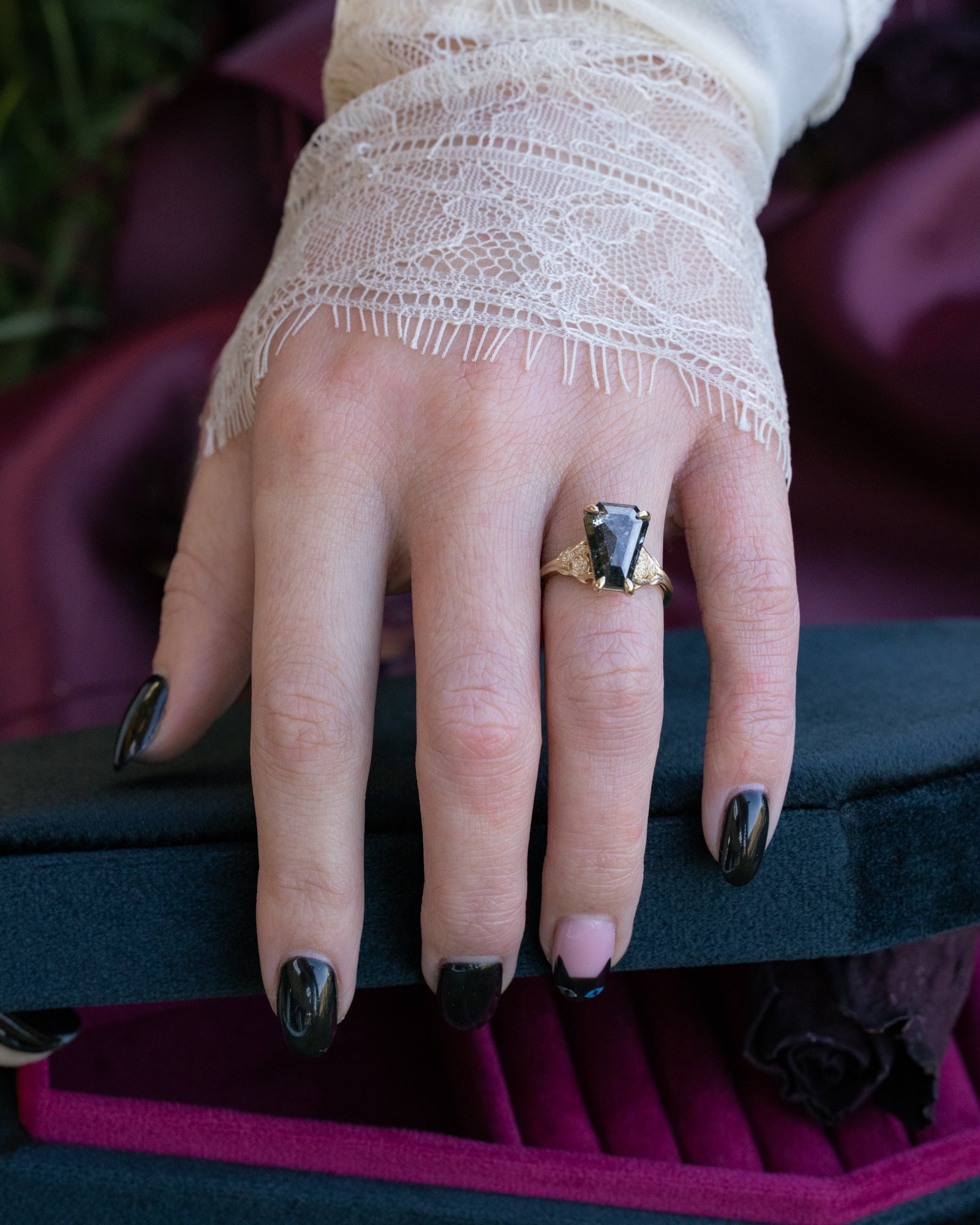 Hand wearing a gold ring with a salt & pepper diamond on a dark surface