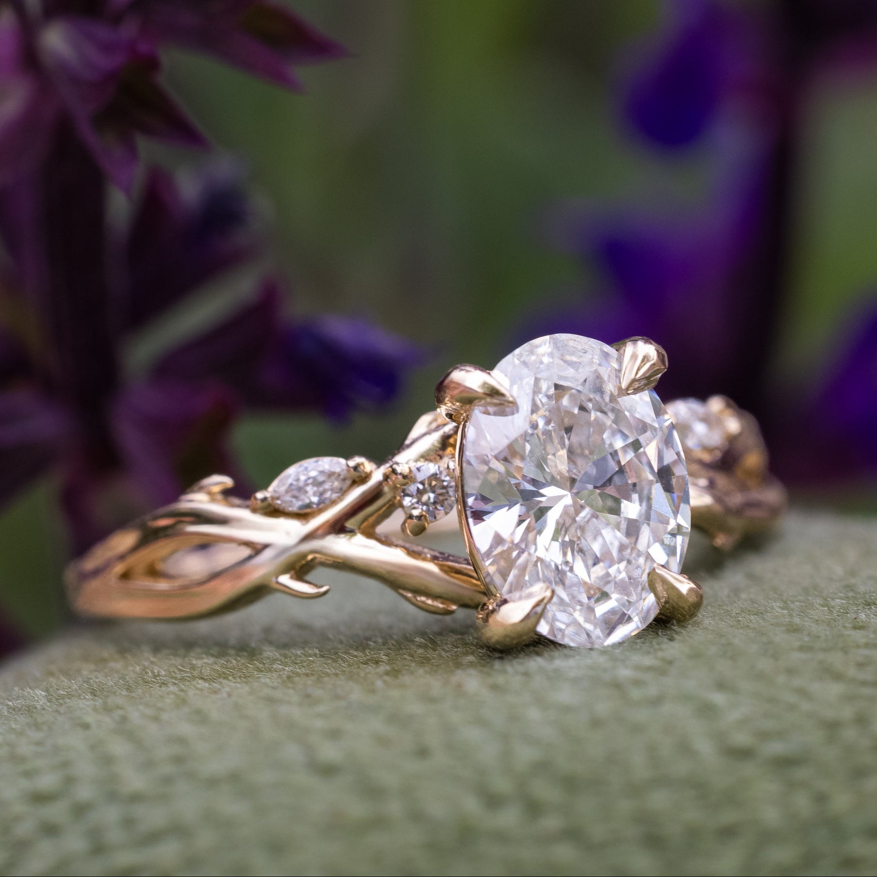 Gold ring with a large diamond on a green surface with purple flowers in the background