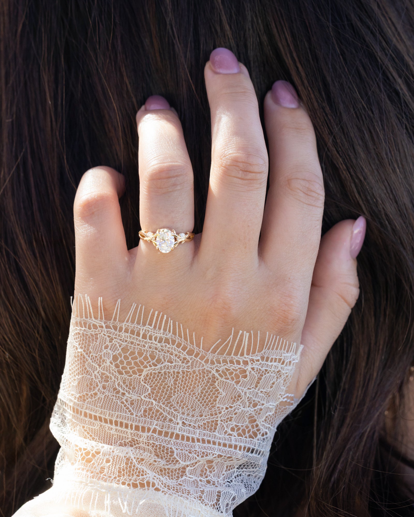 Lace sleeved hand wearing engagement ring with oval lab-grown diamond and accents gainst dark air