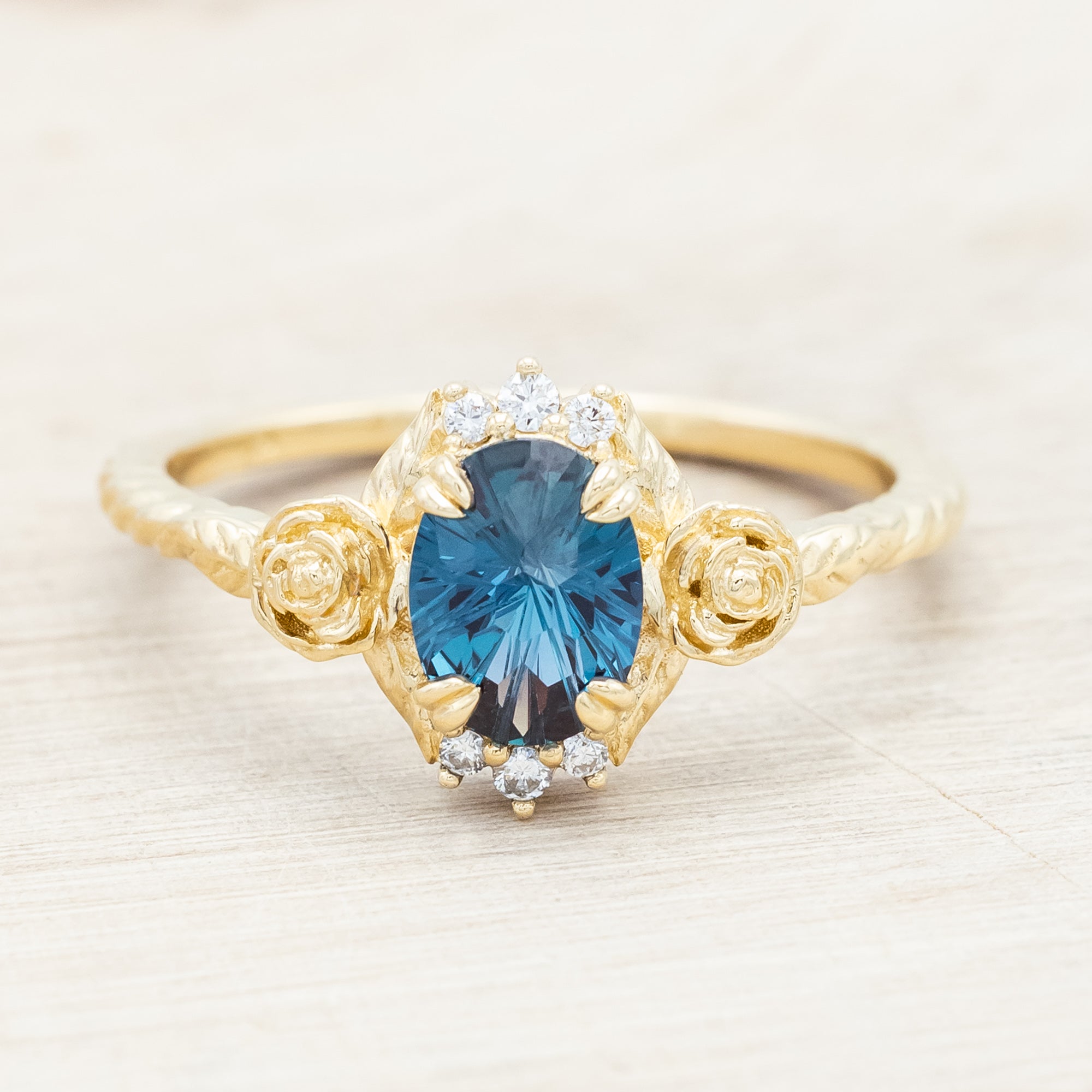 Yellow gold floral-inspired ring with lab alexandrite center stone and diamond accents on a light wooden background