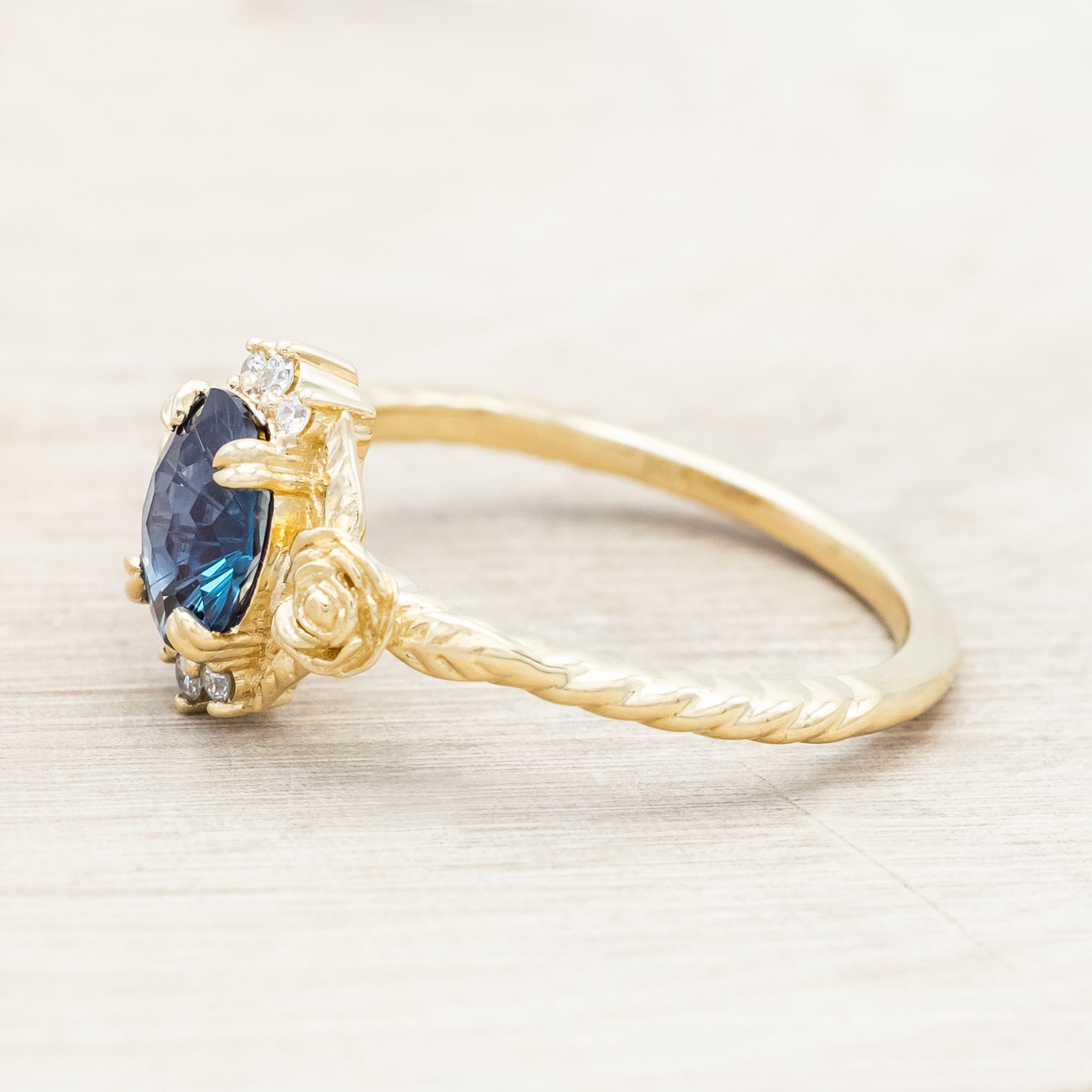 Yellow gold floral-inspired ring with lab alexandrite center stone and diamond accents on a light wooden background