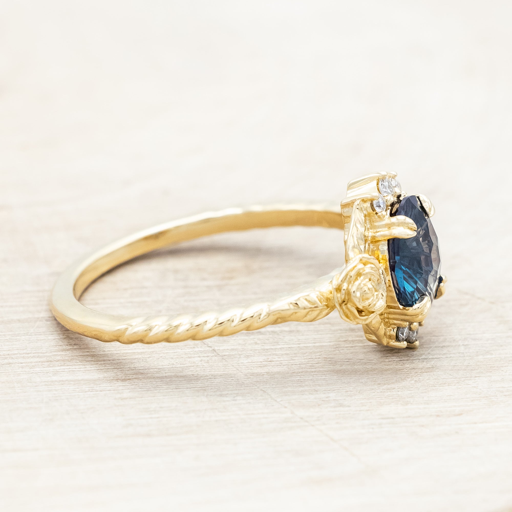 Yellow gold floral-inspired ring with lab alexandrite center stone and diamond accents on a light wooden background