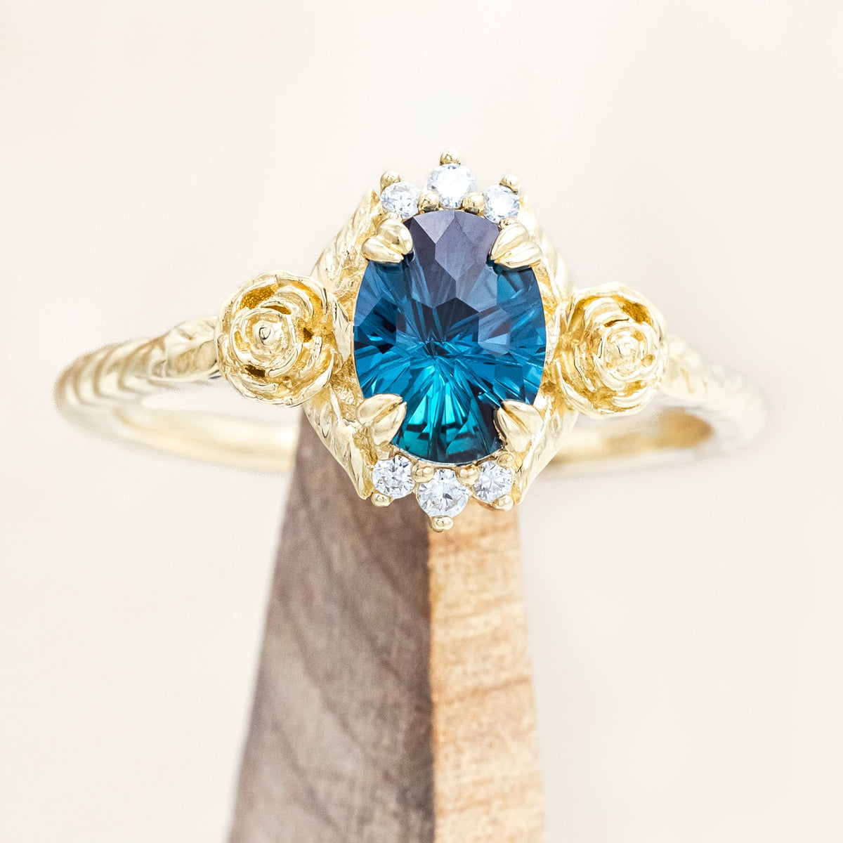 Yellow gold floral-inspired ring with lab alexandrite center stone and diamond accents on a wooden stand