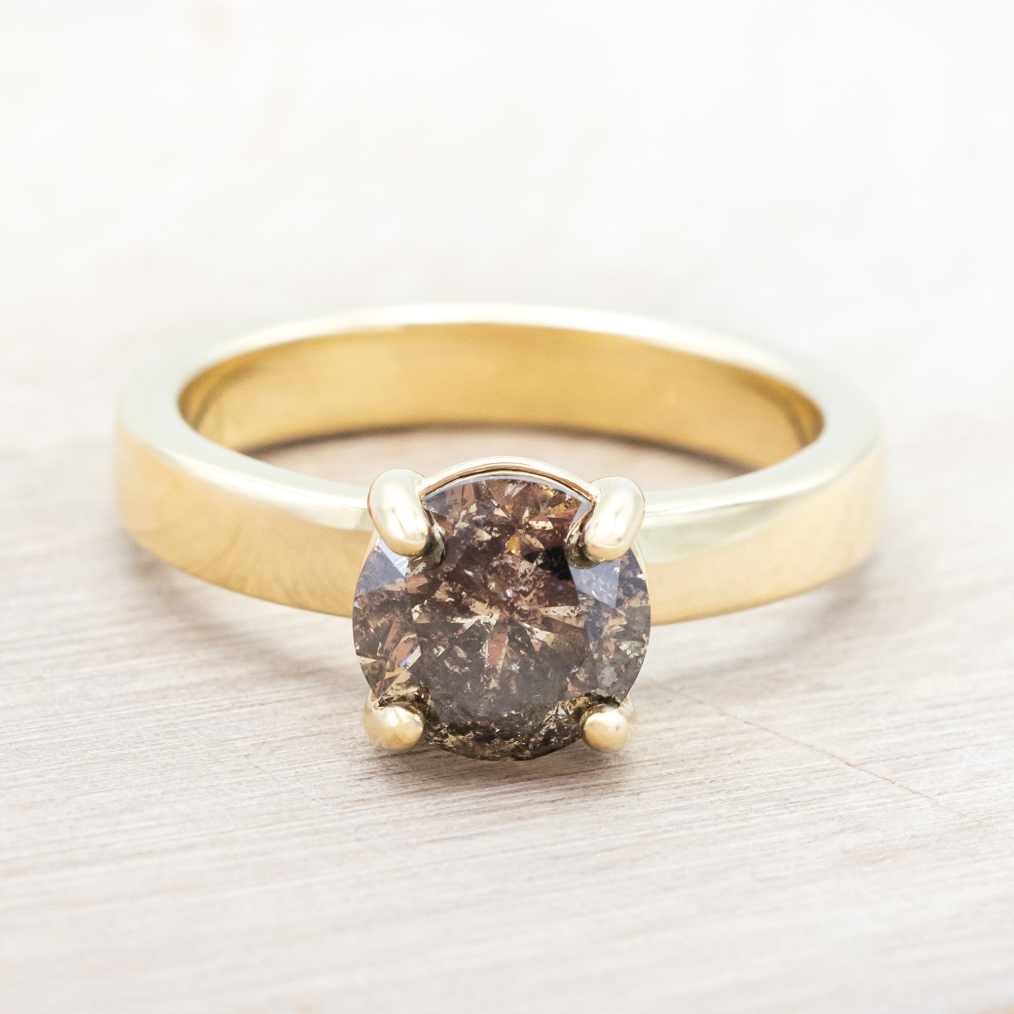 Wide 14K gold ring with a salt & pepper diamond on a beige background