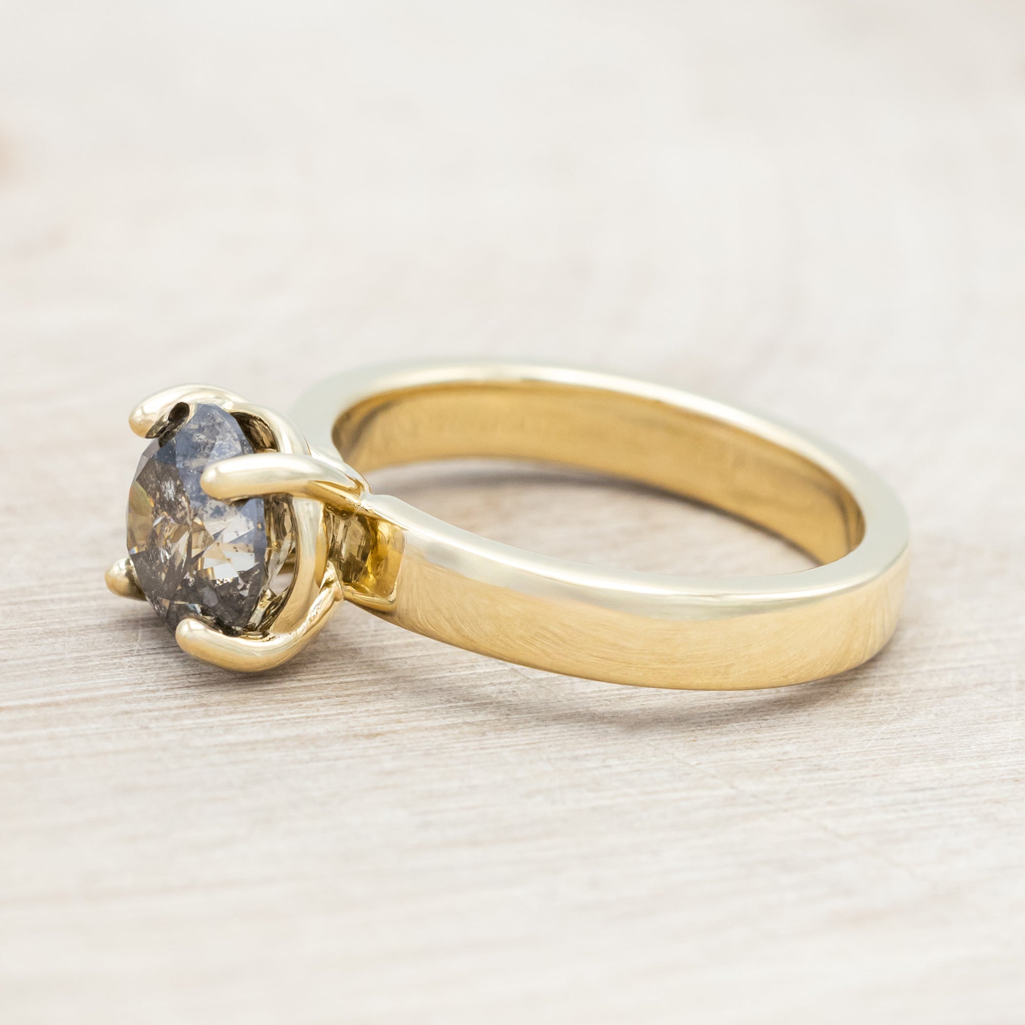 Wide 14K gold ring with a salt & pepper diamond on a beige background