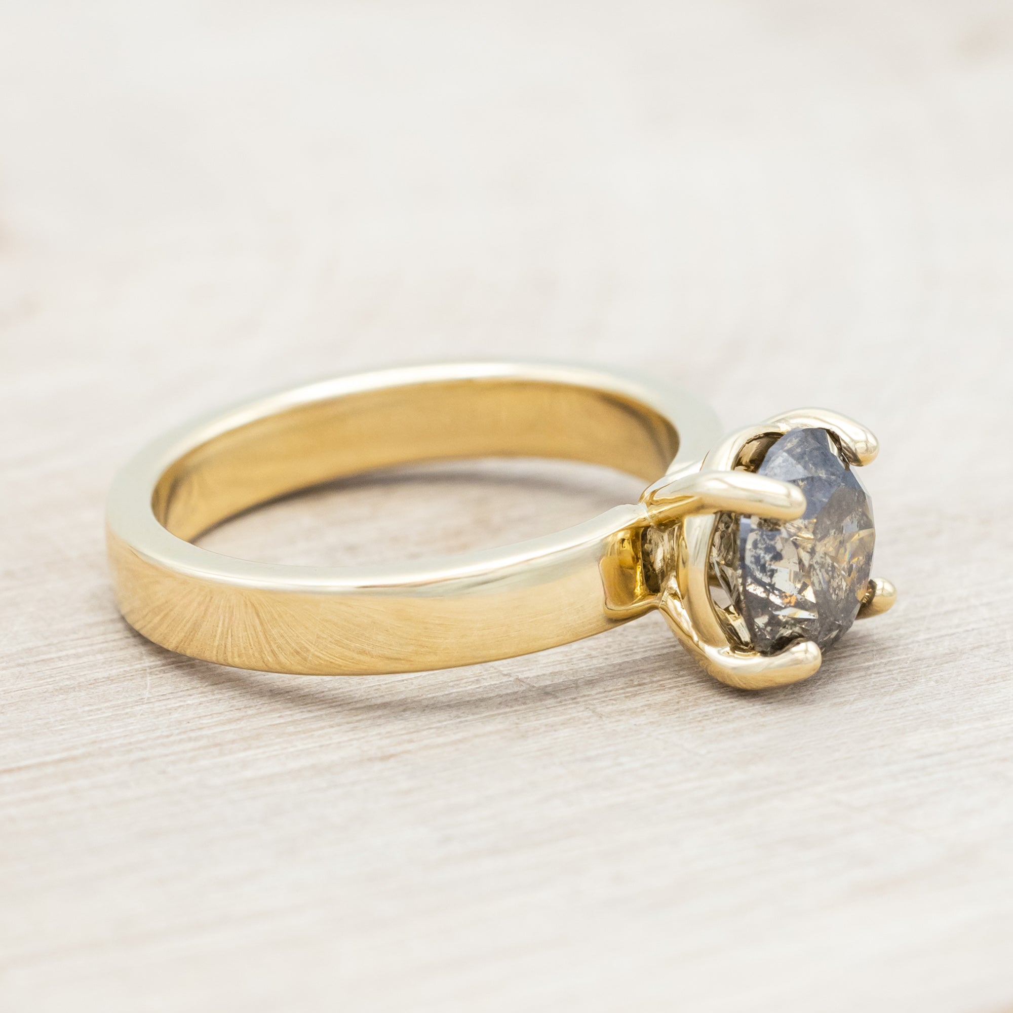 Wide 14K gold ring with a salt & pepper diamond on a beige background
