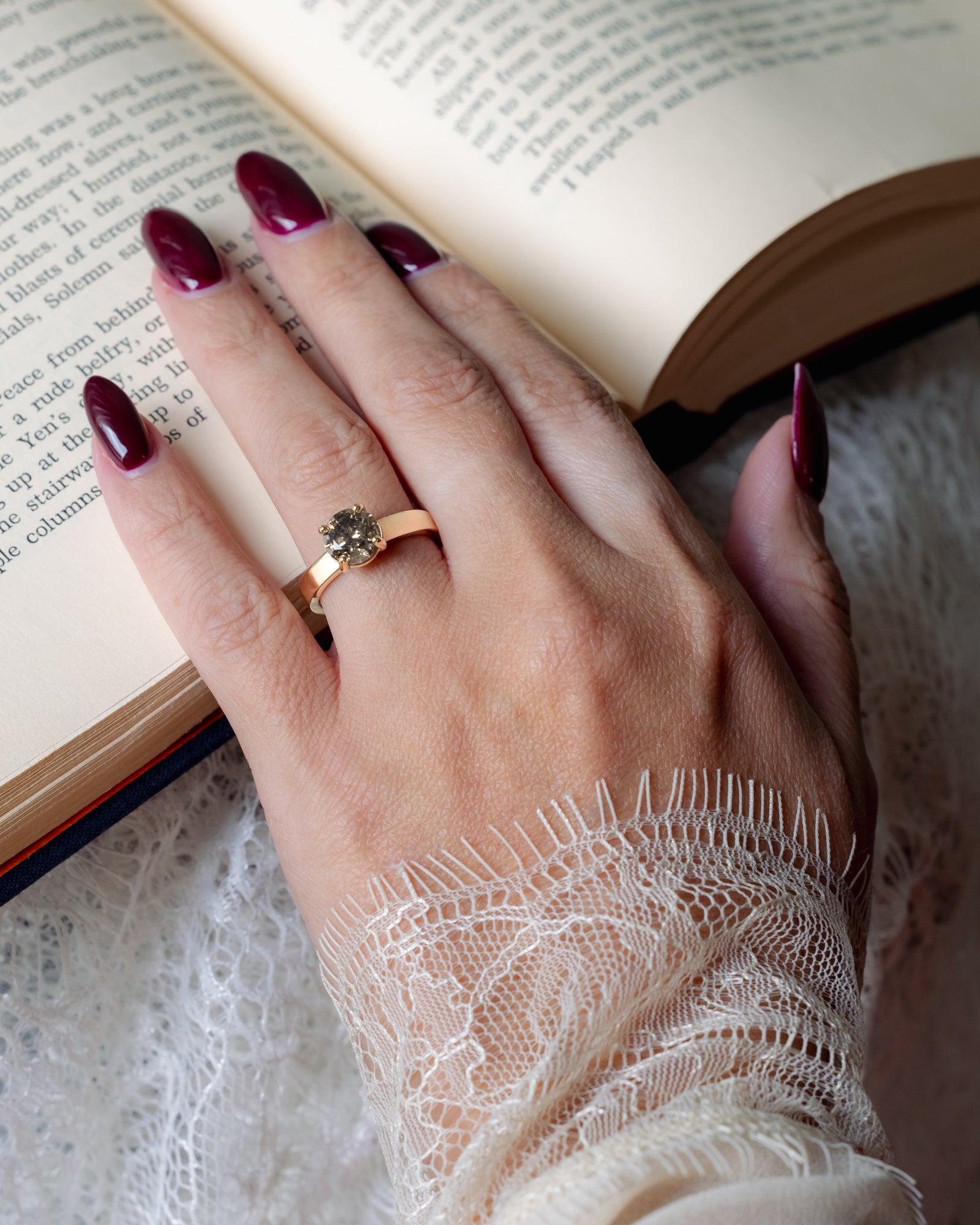 Hand with a salt & pepper ring on a lace sleeve resting on an open book