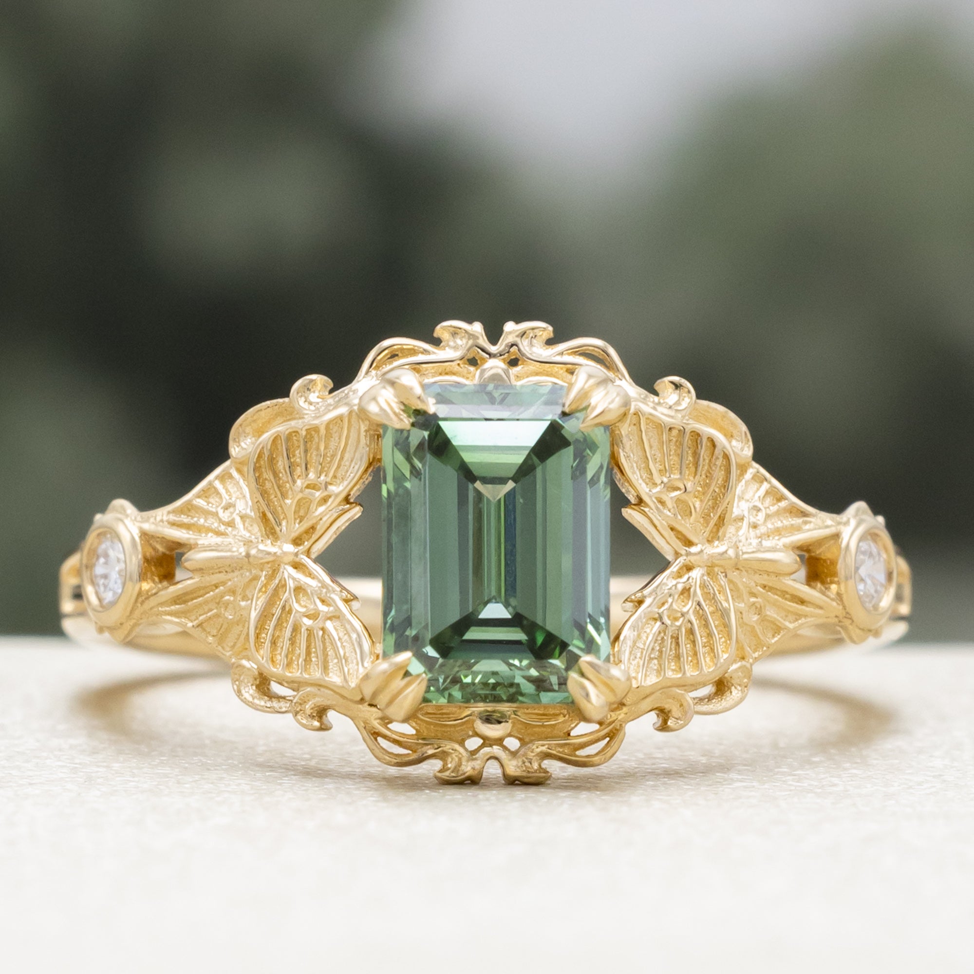 Gold ring with a green lab diamond, moth filigree, and diamond accents on a neutral background