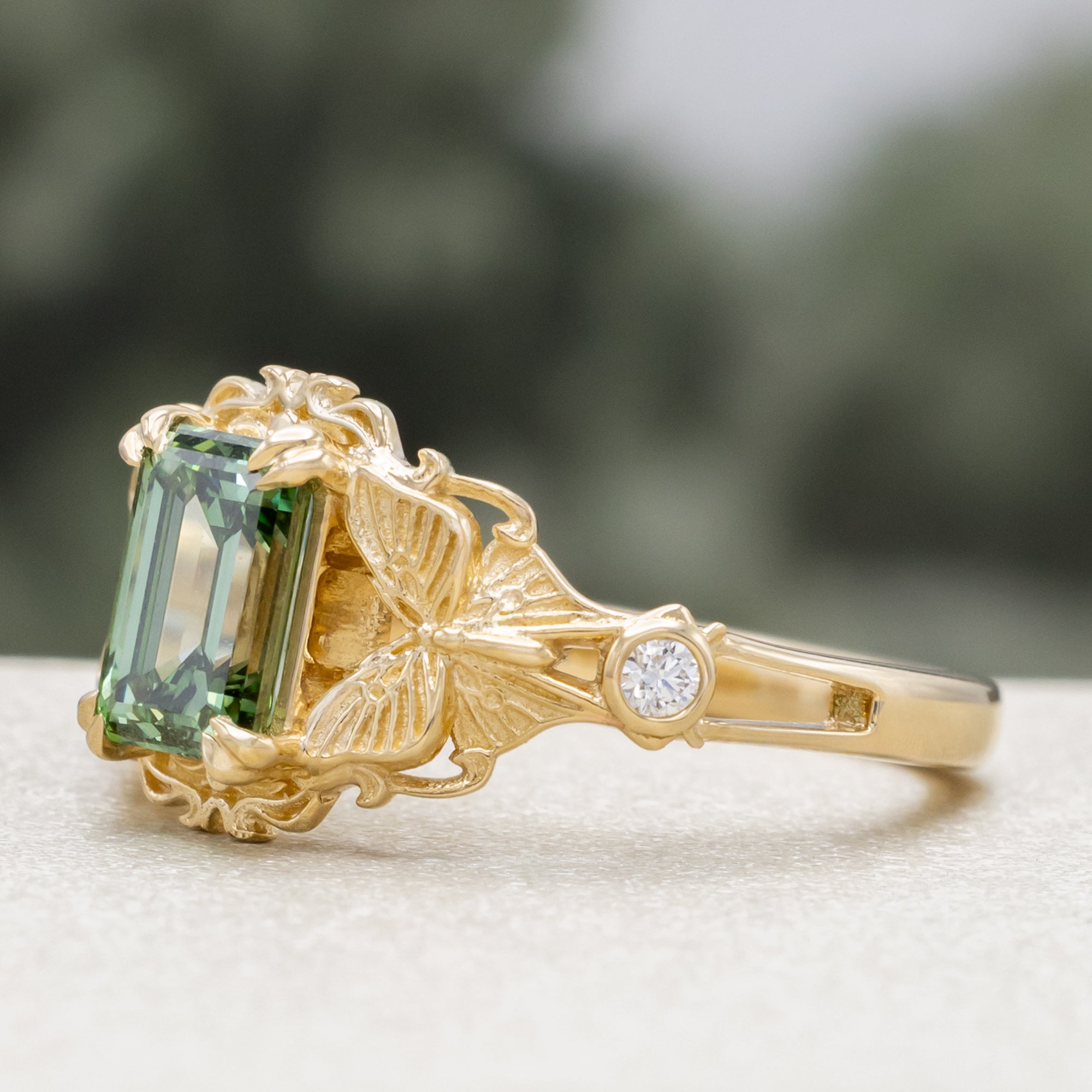Gold ring with a green lab diamond, moth filigree, and diamond accents on a neutral background