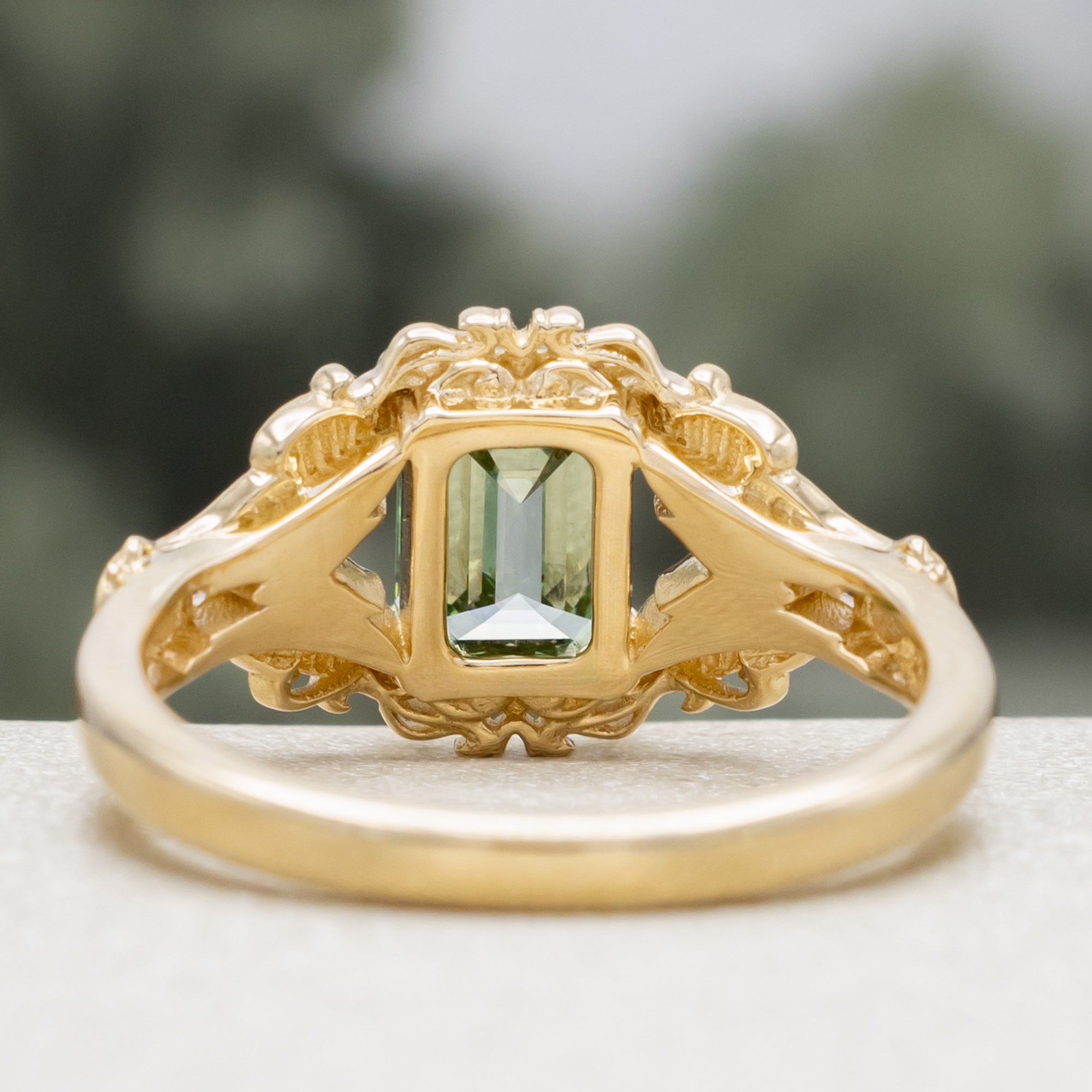 Gold ring with a green lab diamond, moth filigree, and diamond accents on a neutral background