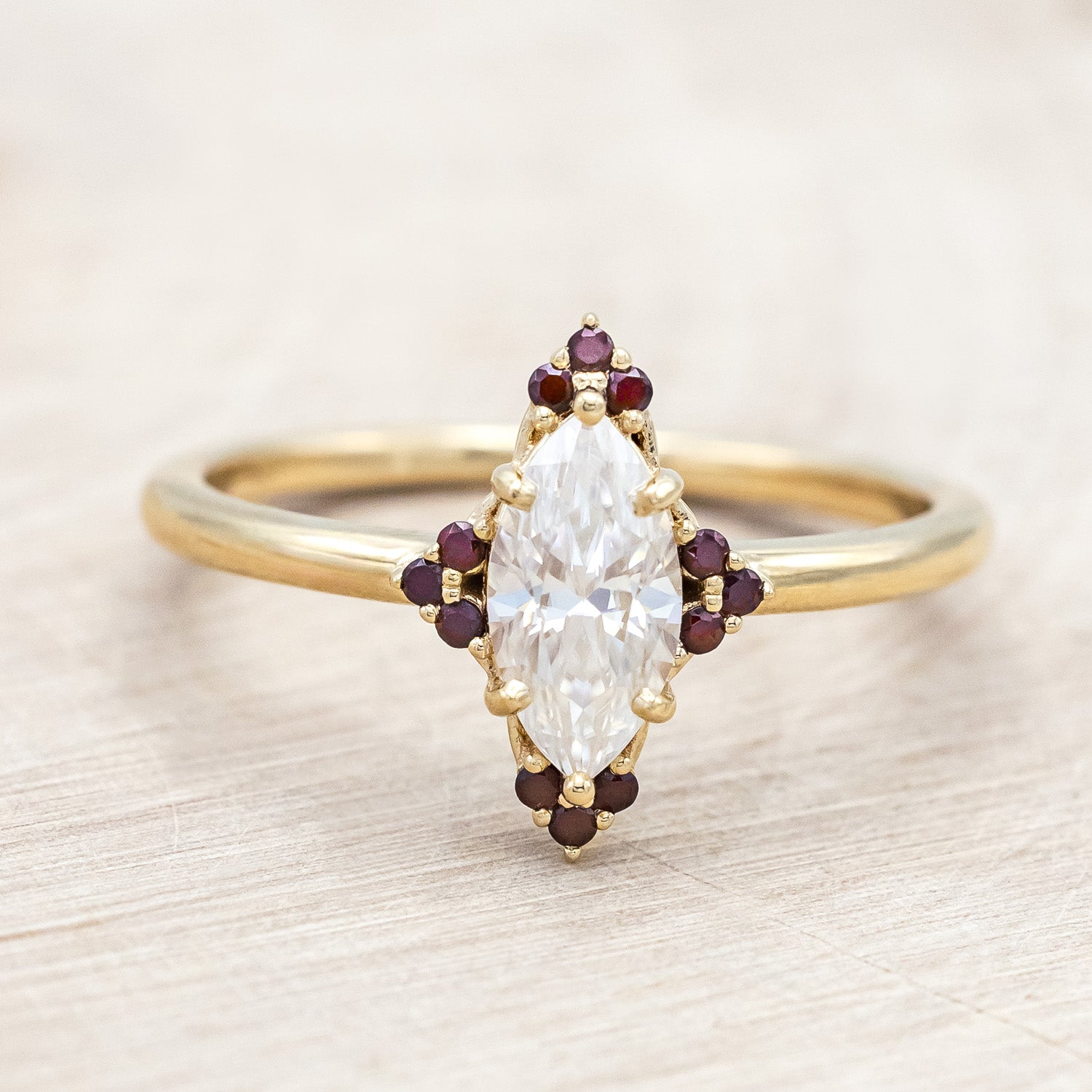 14K gold ring with Moissanite center stone and smaller red garnets on a light background