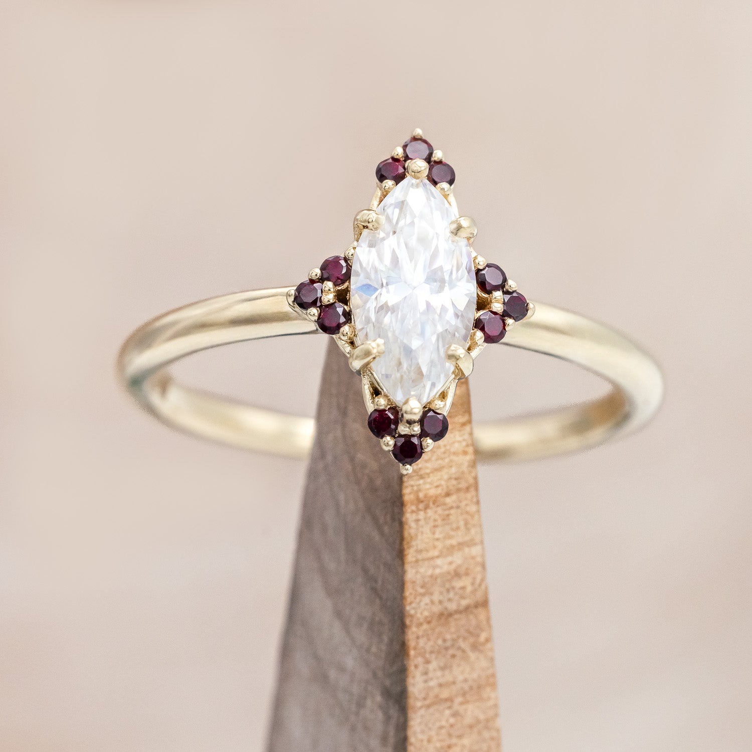 14K gold ring with Moissanite center stone and smaller red garnets on a beige background