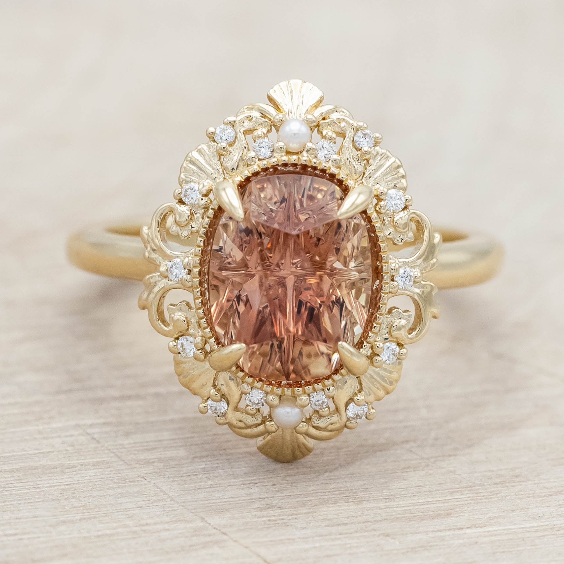 14K yellow gold ring featuring an orange sunstone with small pearls and diamonds on light wooden surface