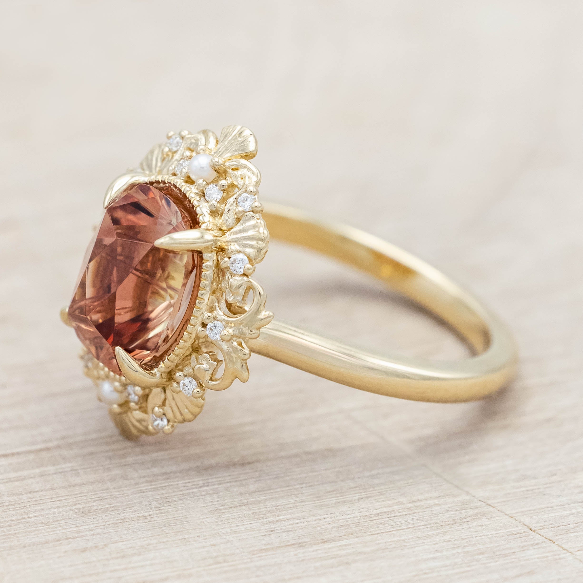 14K yellow gold ring featuring an orange sunstone with small pearls and diamonds on light wooden surface
